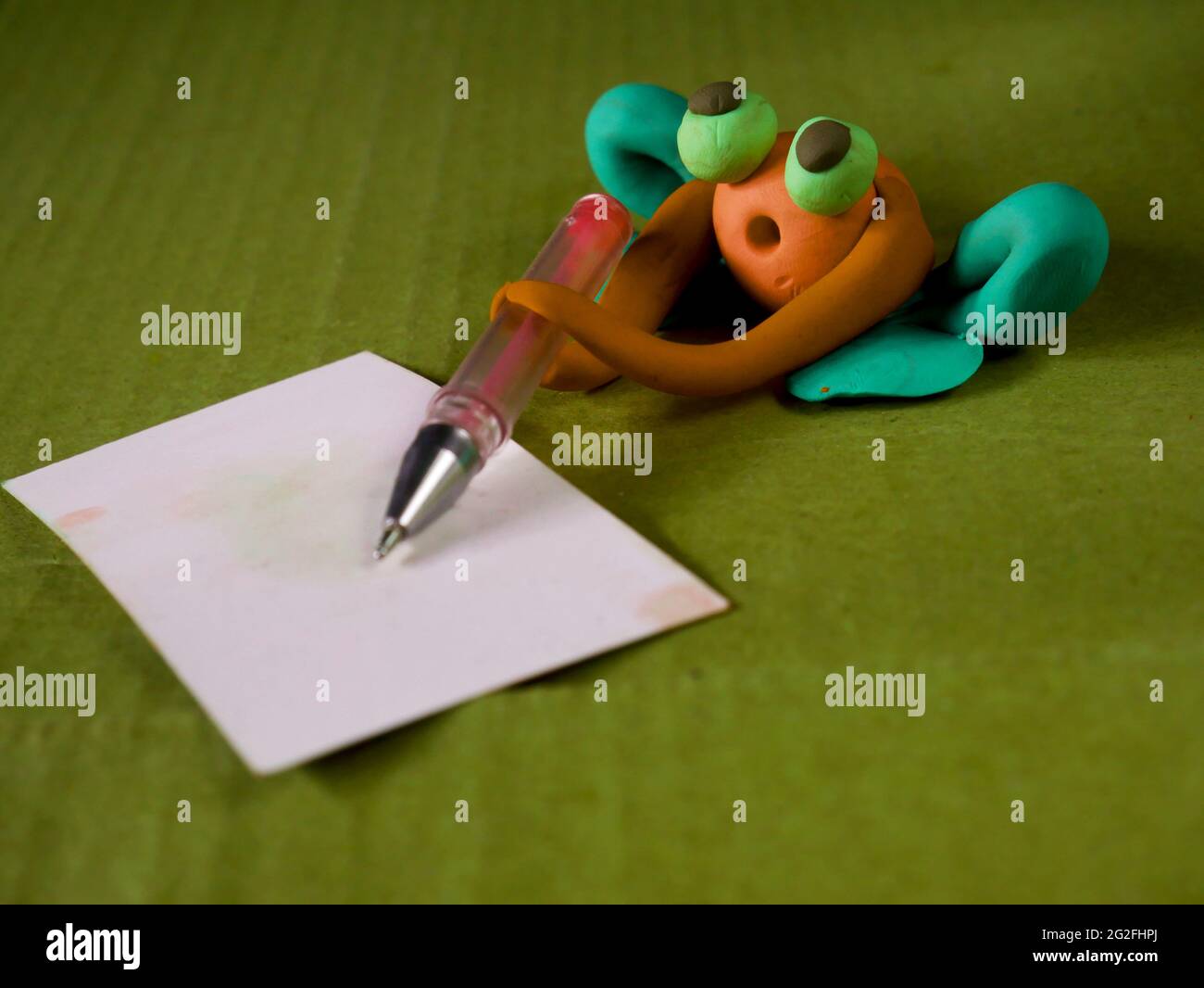 Drôle de grenouille d'argile tenant stylo écriture sur le concept d'éducation de carte blanche Banque D'Images