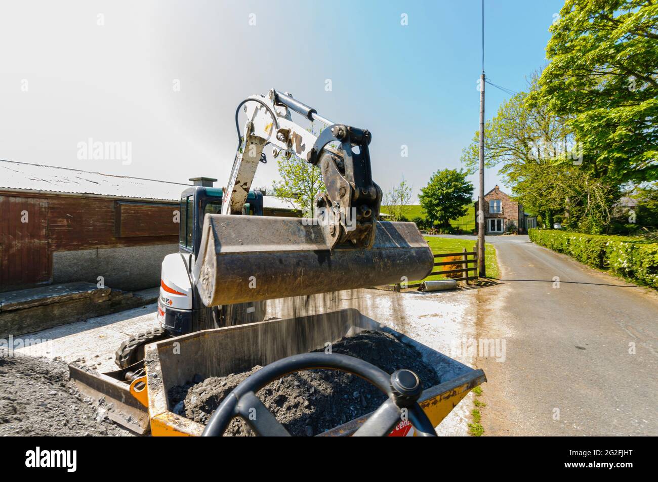 La minipelle Bobcat E25 charge des pierres granulées broyées dans un camion à benne jaune sur un chantier de construction d'une ferme. Banque D'Images