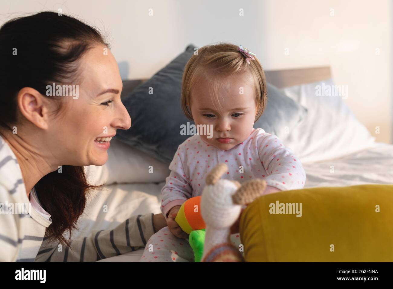 La mère caucasienne et son bébé jouent avec un jouet tout en étant assis sur le lit à la maison Banque D'Images