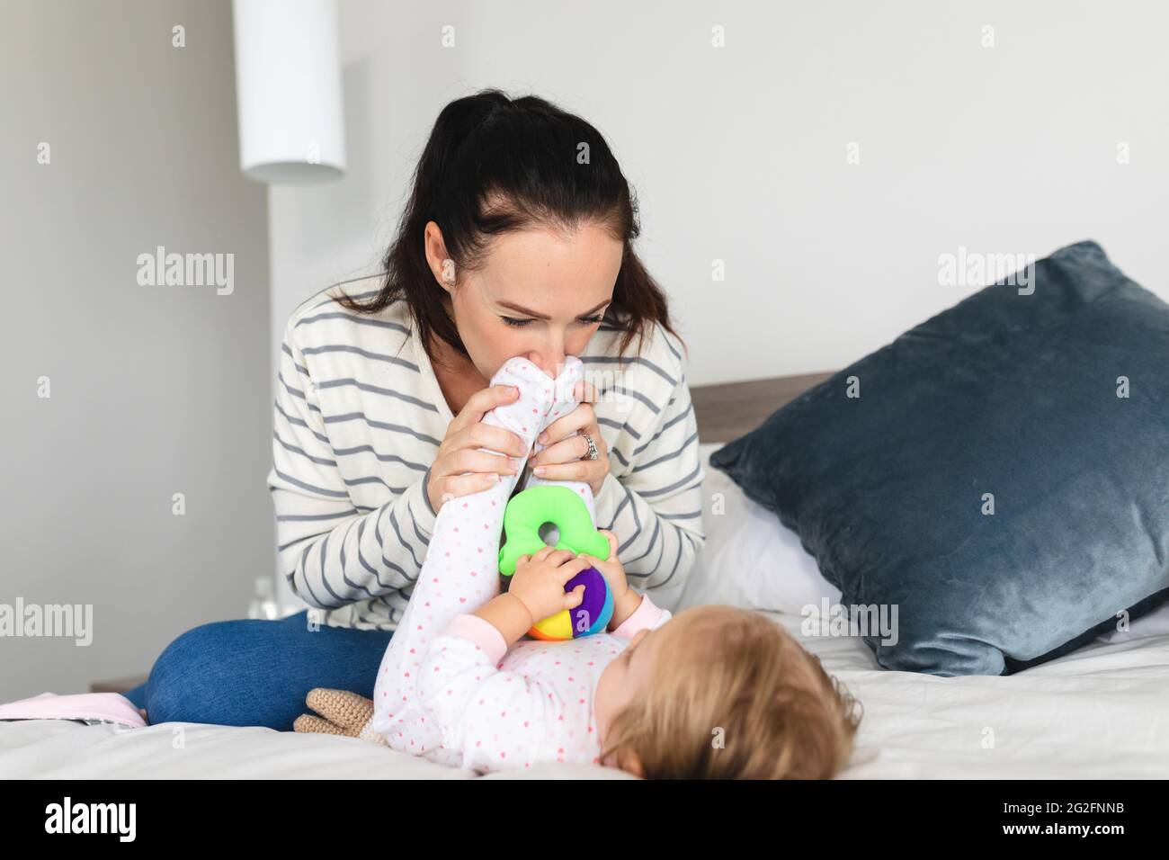 La mère caucasienne embrasse les pieds de son bébé tout en étant assise sur le lit à la maison Banque D'Images