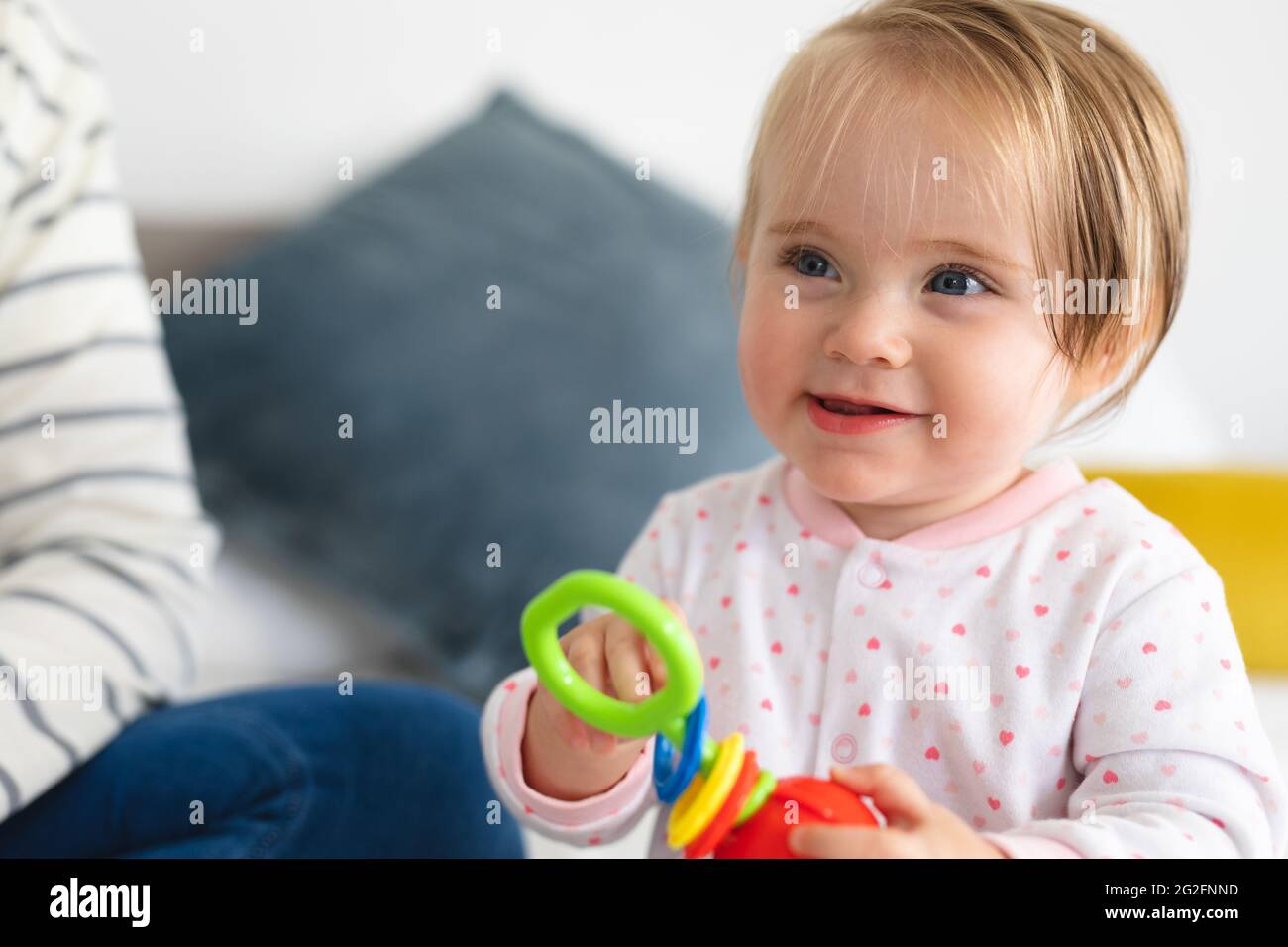 Bébé caucasien souriant en jouant avec un jouet assis sur le lit à la maison Banque D'Images