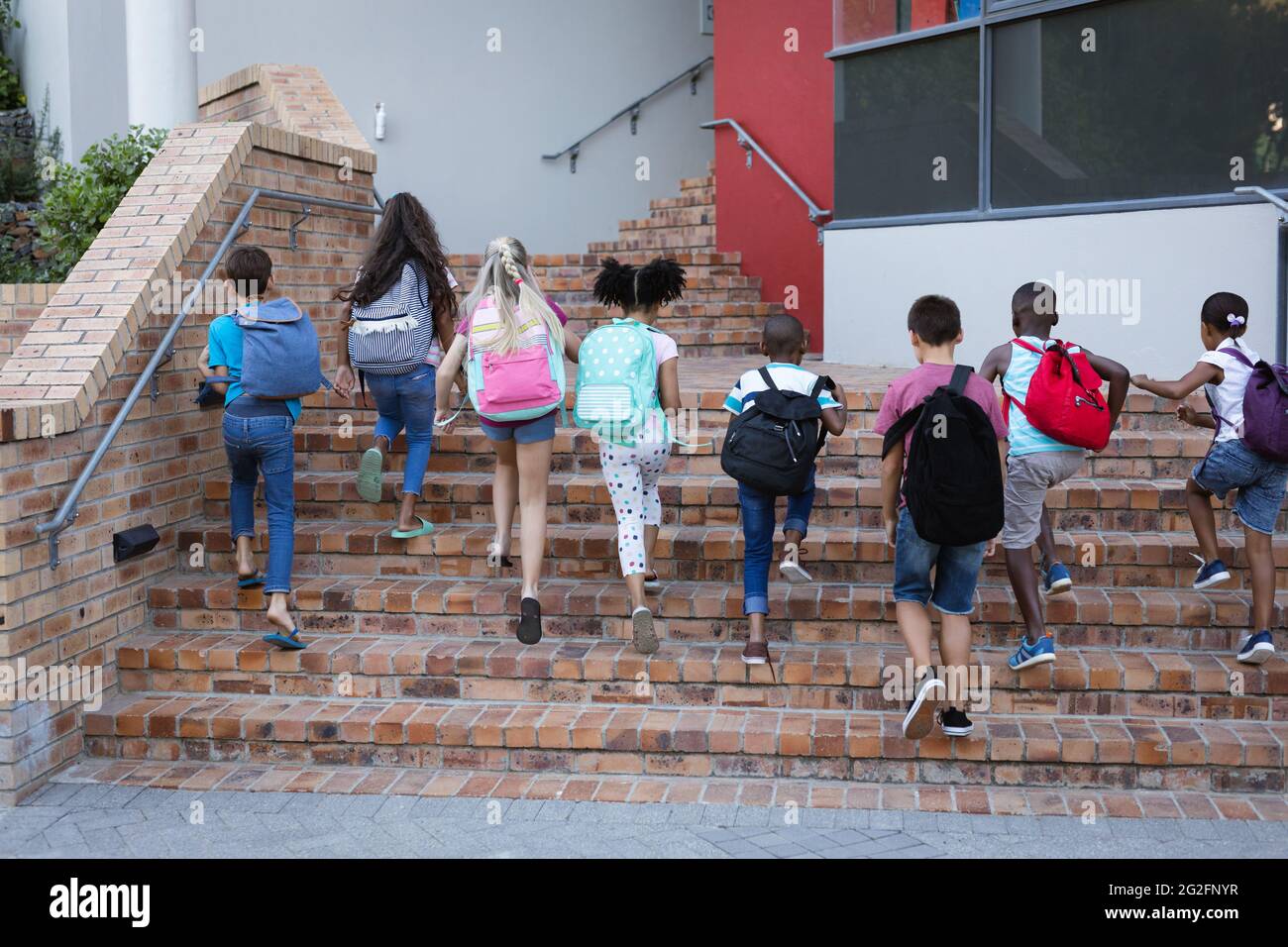 Vue arrière d'un groupe d'élèves divers avec des sacs à dos montant les escaliers ensemble à l'école Banque D'Images