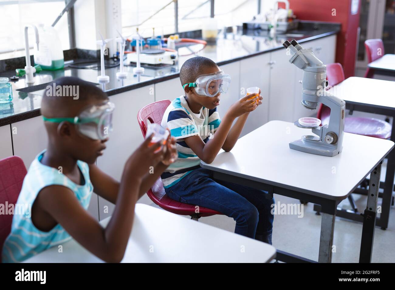 Deux garçons afro-américains portant des lunettes de protection tenant un bécher en classe scientifique au laboratoire Banque D'Images