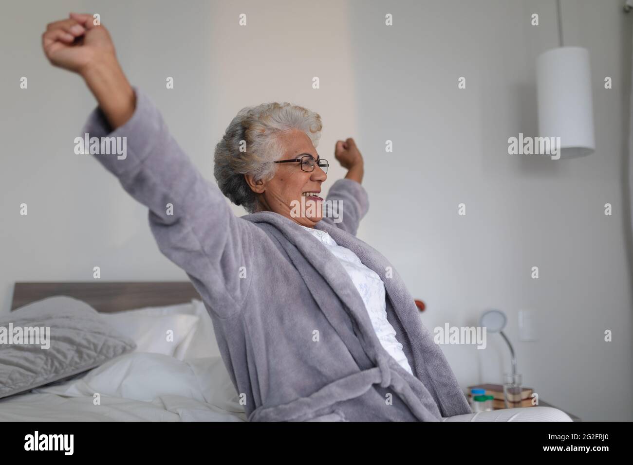 Femme âgée de race mixte assise sur le lit élargissant ses bras Banque D'Images