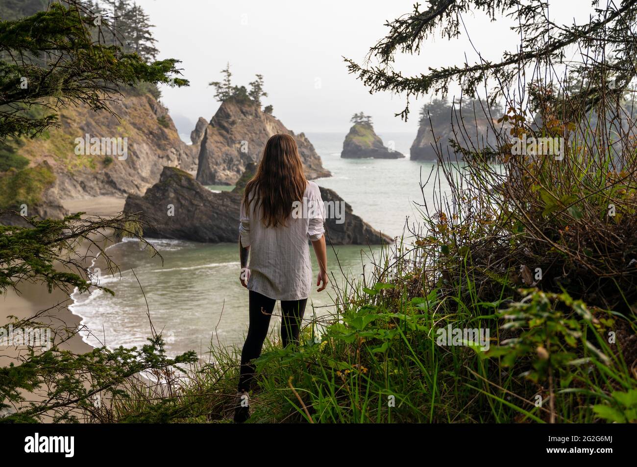 Femme portant une chemise blanche encadrée par des arbres et des piles de la mer sur la côte Banque D'Images