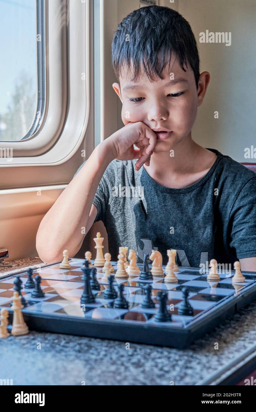 Un garçon asiatique réfléchit à un mouvement dans une partie d'échecs assis dans le train Banque D'Images