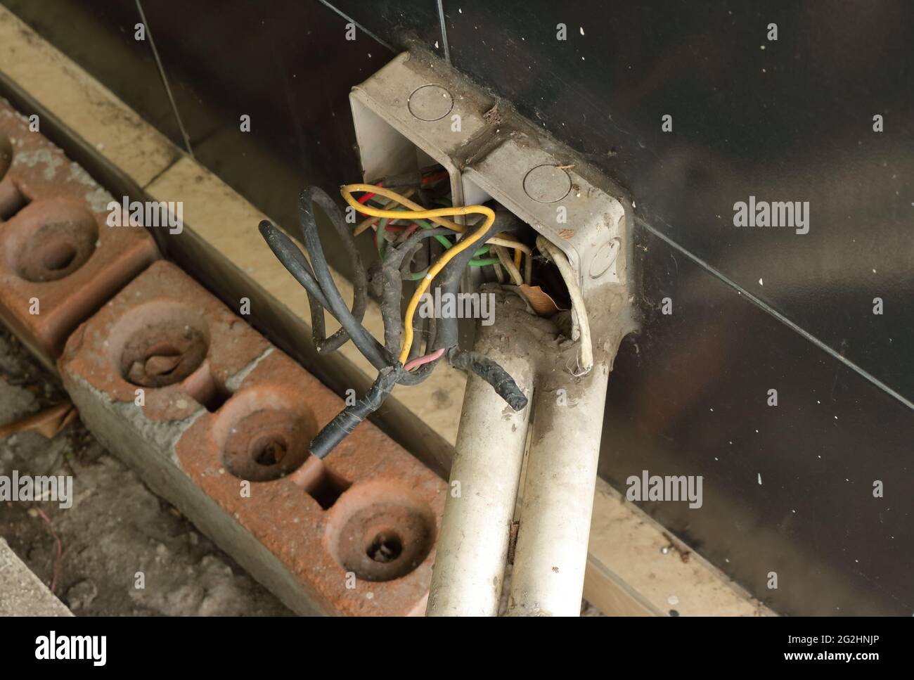 Gros plan des fils électriques dans les boîtes de jonction non découvertes installées sur un mur en carreaux noirs près du sol, vue à angle élevé Banque D'Images