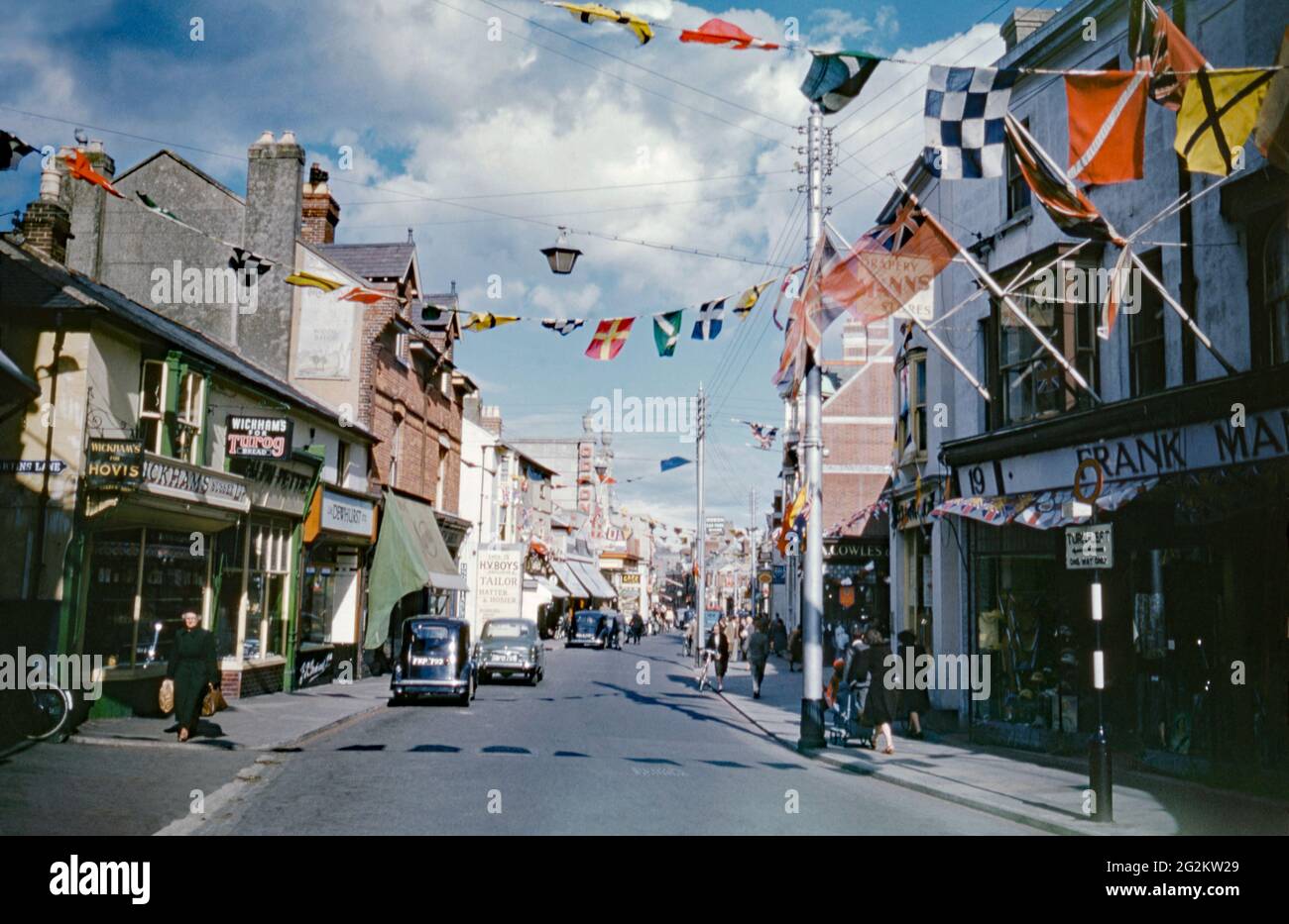 Il y a des banderoles colorées de l'autre côté de la rue et des drapeaux syndicaux volant dans High Street, Littlehampton, West Sussex, Angleterre, Royaume-Uni en 1953. C'était pour le couronnement d'Elizabeth II qui a eu lieu le 2 juin 1953 à l'abbaye de Westminster, à Londres. Elizabeth II a accédé au trône à l'âge de 25 ans à la mort de son père, George VI, en 1952. La rue abrite le cinéma Art Deco Odeon (au centre à gauche). Cela a été démoli et la rue est maintenant sans voiture. . Cette image est tirée d'une ancienne transparence couleur Kodak 35 mm amateur, une photographie vintage des années 1950. Banque D'Images