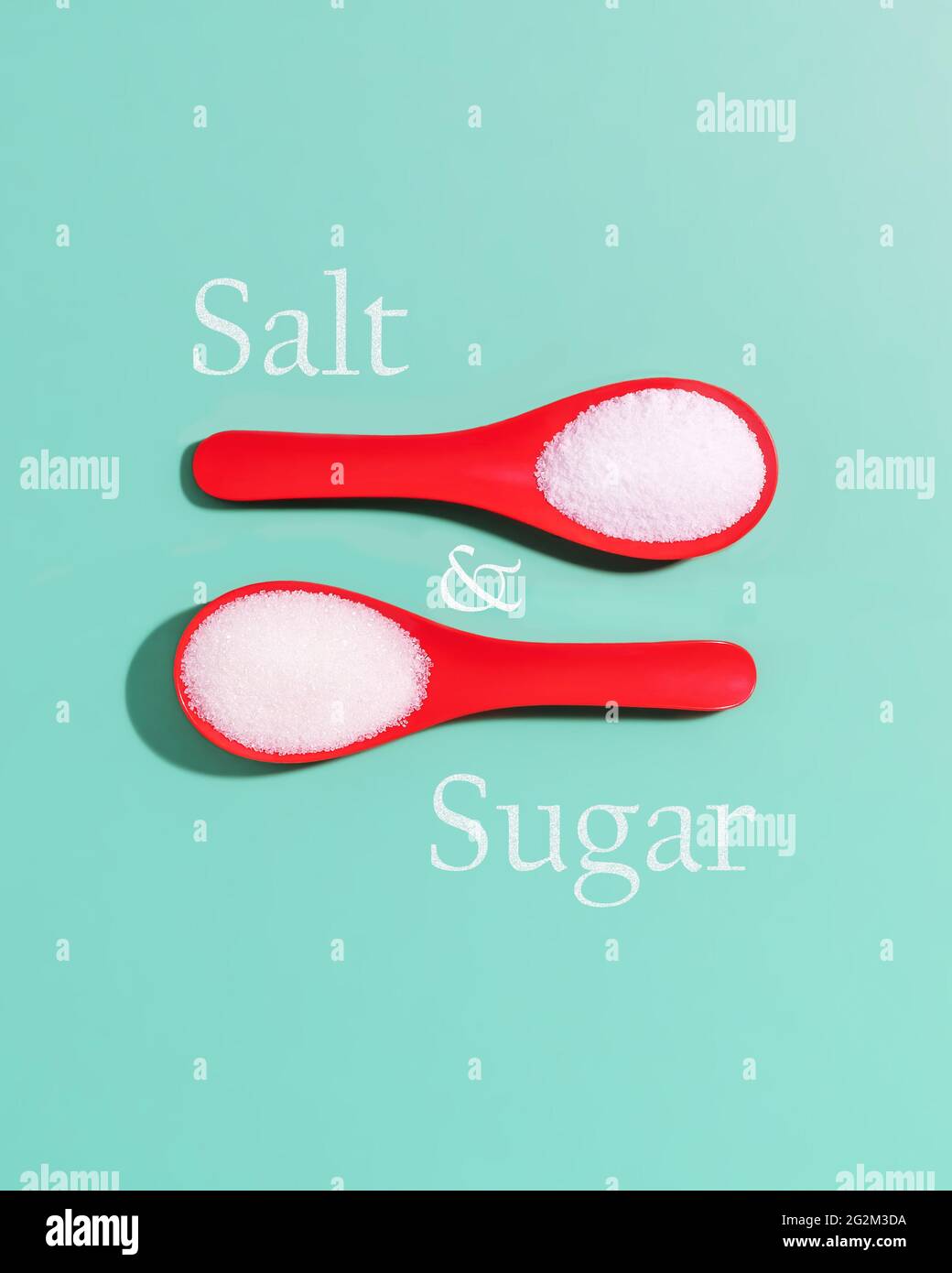 Composition minimaliste contrastée avec sel de mer et sucre dans des cuillères en plastique rouge et inscription sucre et sel sur fond bleu clair Banque D'Images