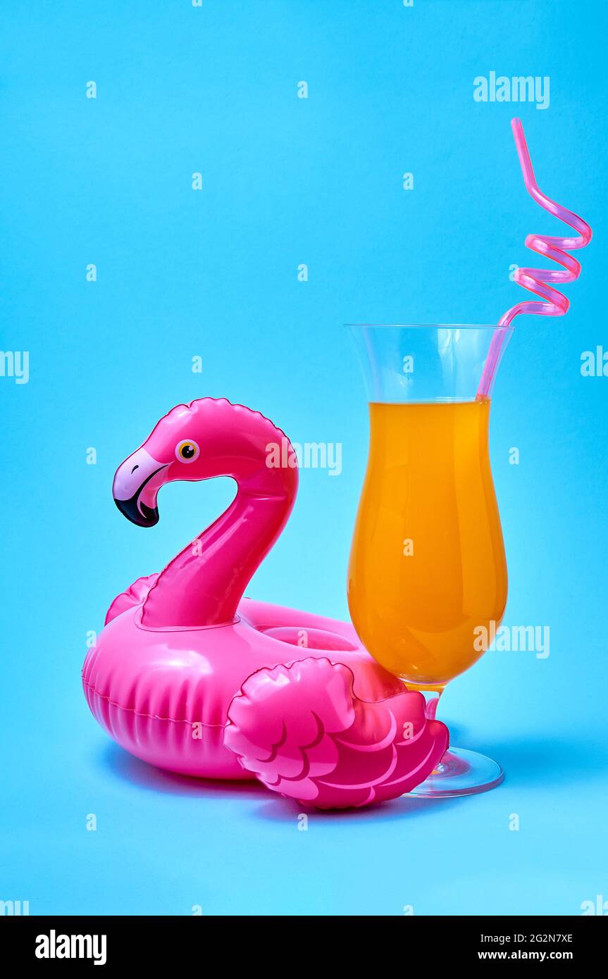 Cocktail tequila lever du soleil avec jouet gonflable rose flamants de piscine sur fond bleu. Concept été créatif. Banque D'Images