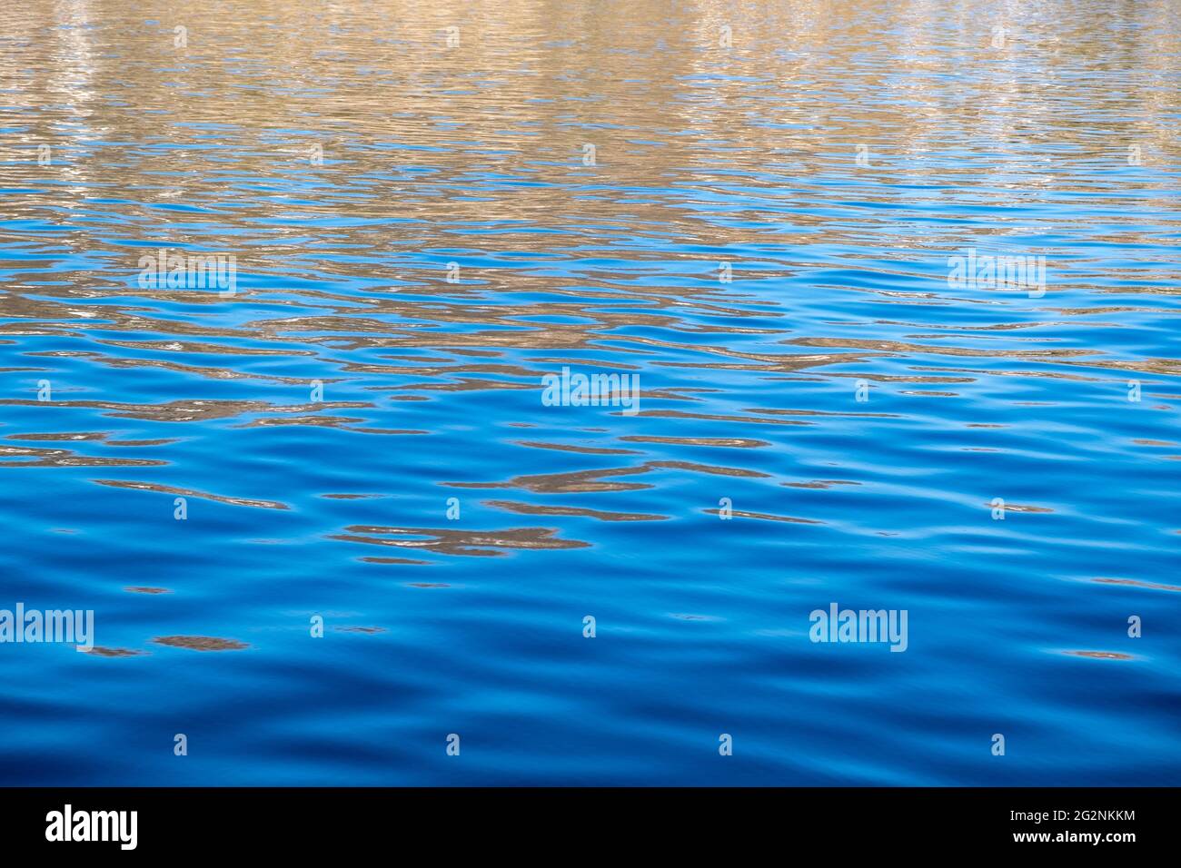 Surface d'eau de mer calme avec de petites ondulations, fond bleu profond, reflets dorés. Paysage marin tranquille, espace Banque D'Images