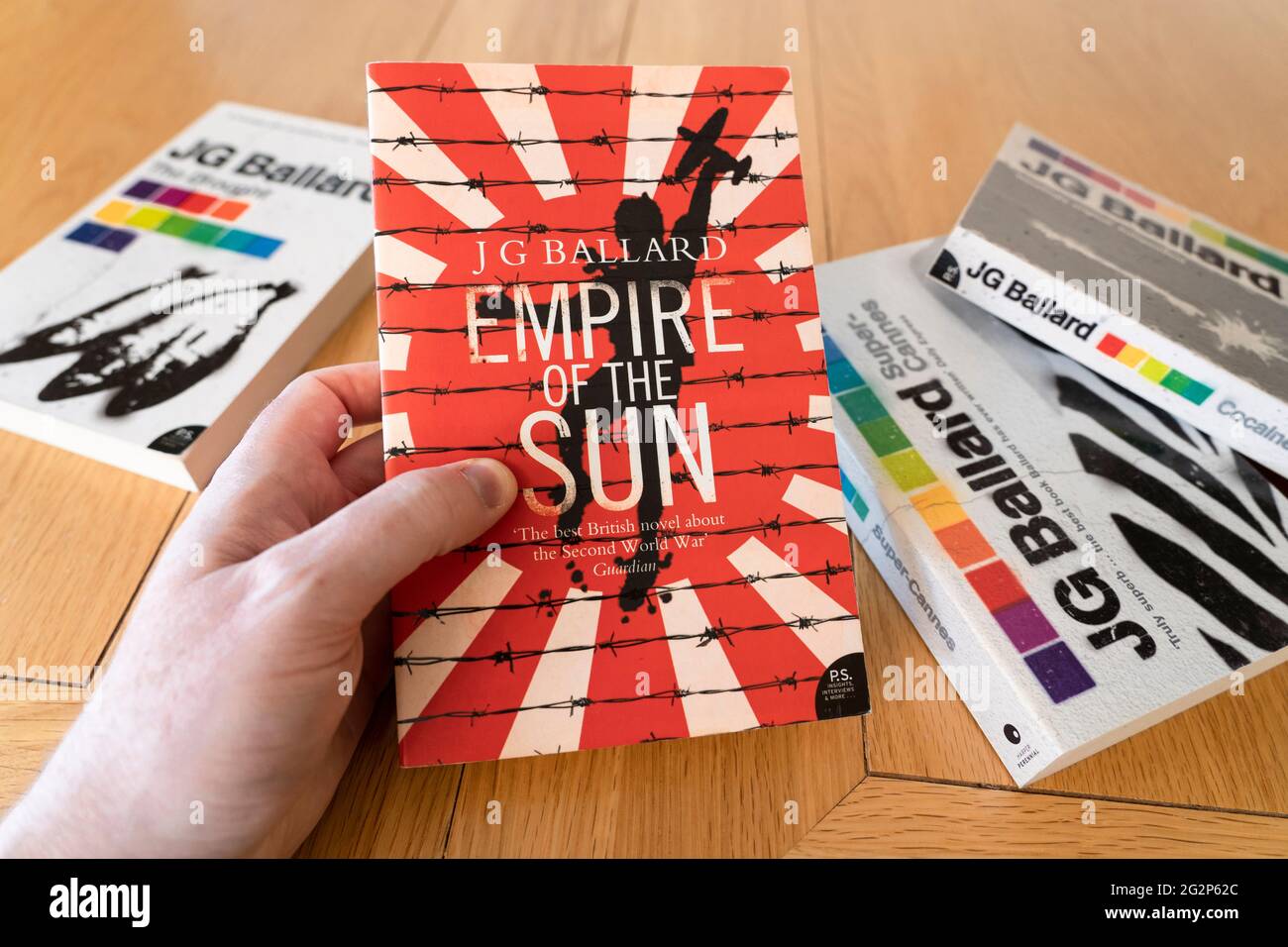 Main d'un homme tenant un livre de poche de l'Empire du Soleil, un roman de l'époque de la guerre de l'âge de l'auteur anglais J. G. Ballard Banque D'Images