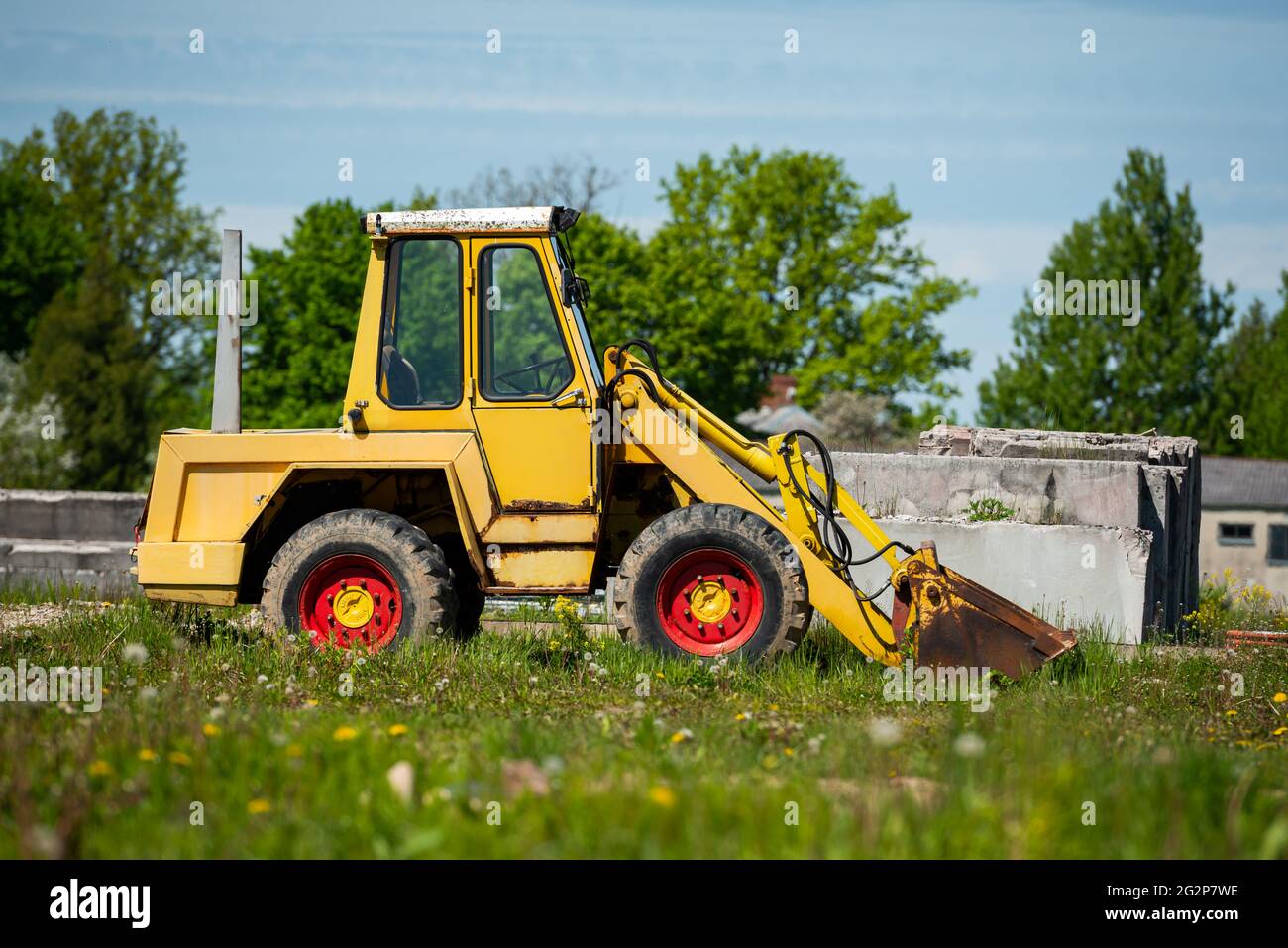 Pelle hydraulique jaune avec disques rouges sur une herbe verte contre le ciel bleu Banque D'Images