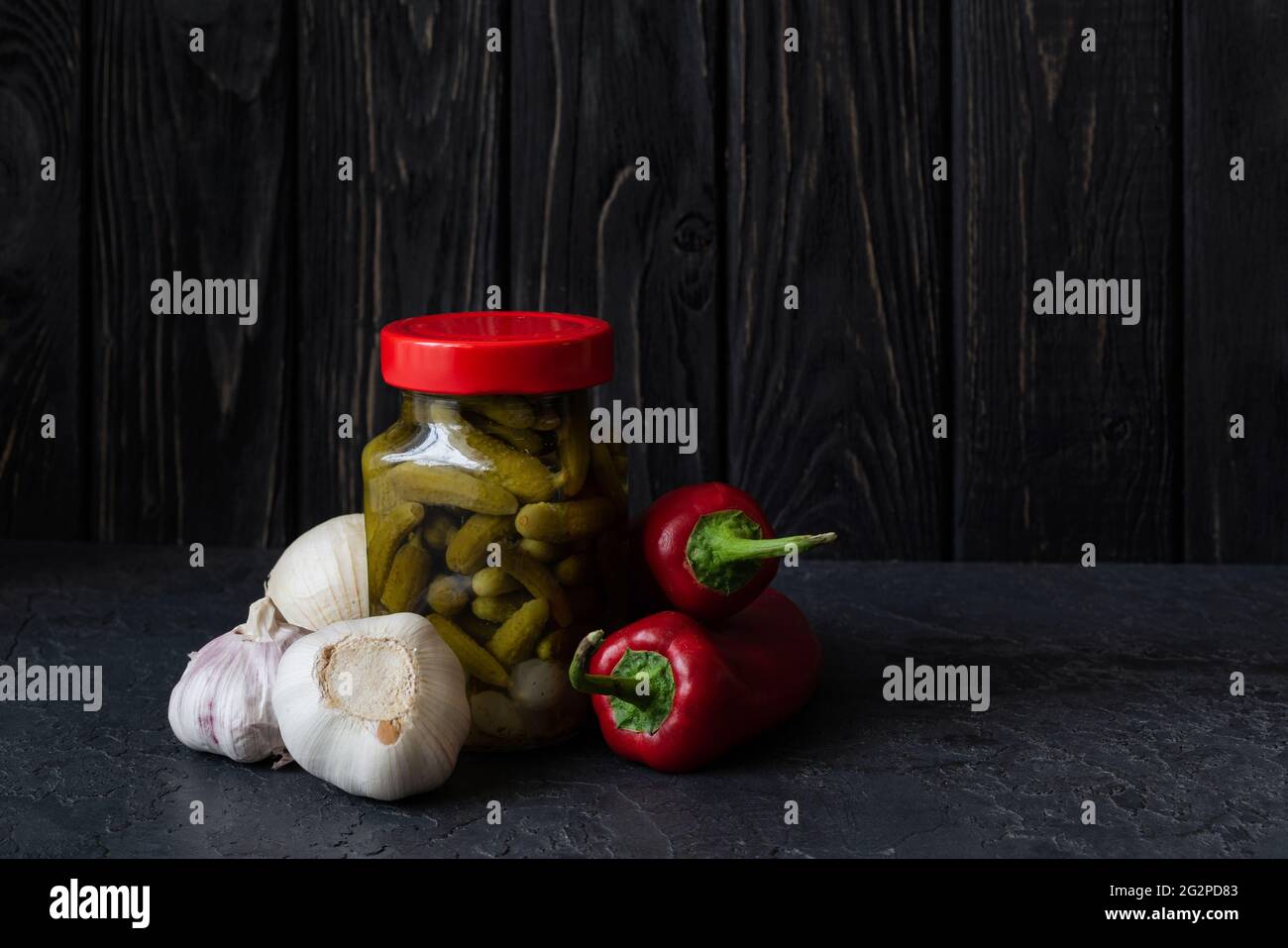 Concombres fermentés, poivron rouge et ail sur fond sombre. Plats végétariens. Concombres salés. Concombres biologiques marinés. Plats fermentés faits maison Banque D'Images