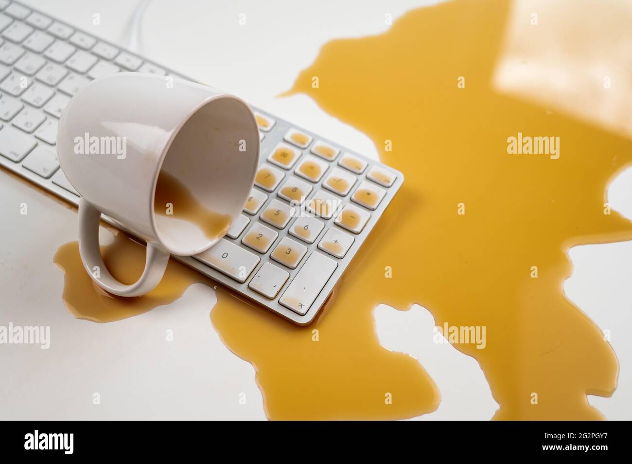 Tasse de café noir renversée sur le clavier de l'ordinateur sur la table blanche. Banque D'Images Tasse de café noir renversée sur le clavier de l'ordinateur sur la table blanche. Banque D'Images