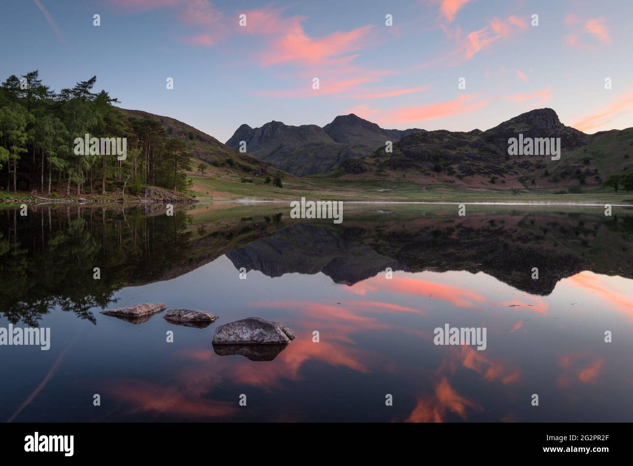 Reflet parfait d'un beau lever de soleil avec des rochers éparpillés en premier plan à Blea Tarn dans le Lake District, Royaume-Uni. Banque D'Images