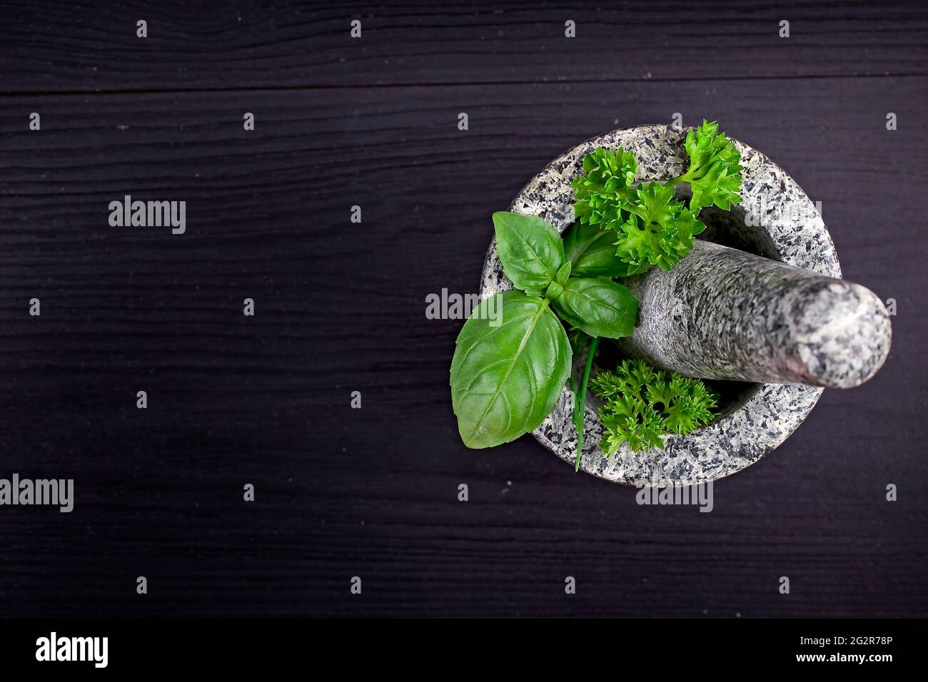 herbes fraîches dans un mortier en pierre sur une table en bois noir Banque D'Images