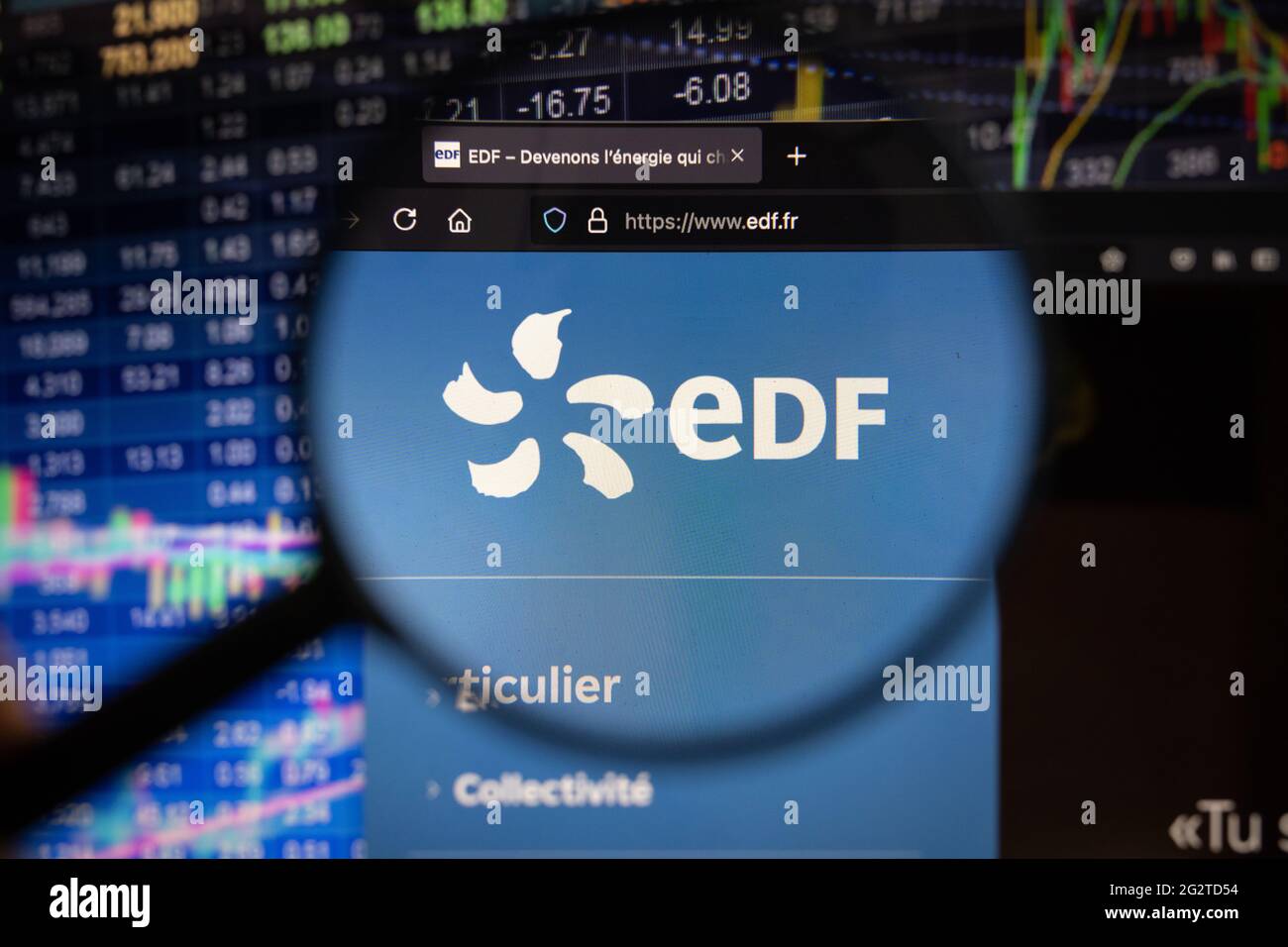 Logo de la société EDF sur un site web avec des développements flous du marché boursier en arrière-plan, vu sur un écran d'ordinateur à travers une loupe Banque D'Images