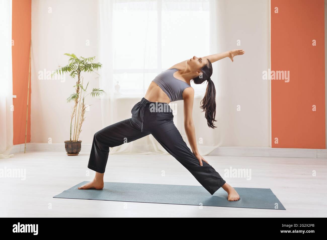 Jeune femme attirante dans les vêtements de sport, pratiquant le yoga, se produit en studio debout sur le tapis, Virabhadrasana exercice, posture du guerrier. Banque D'Images