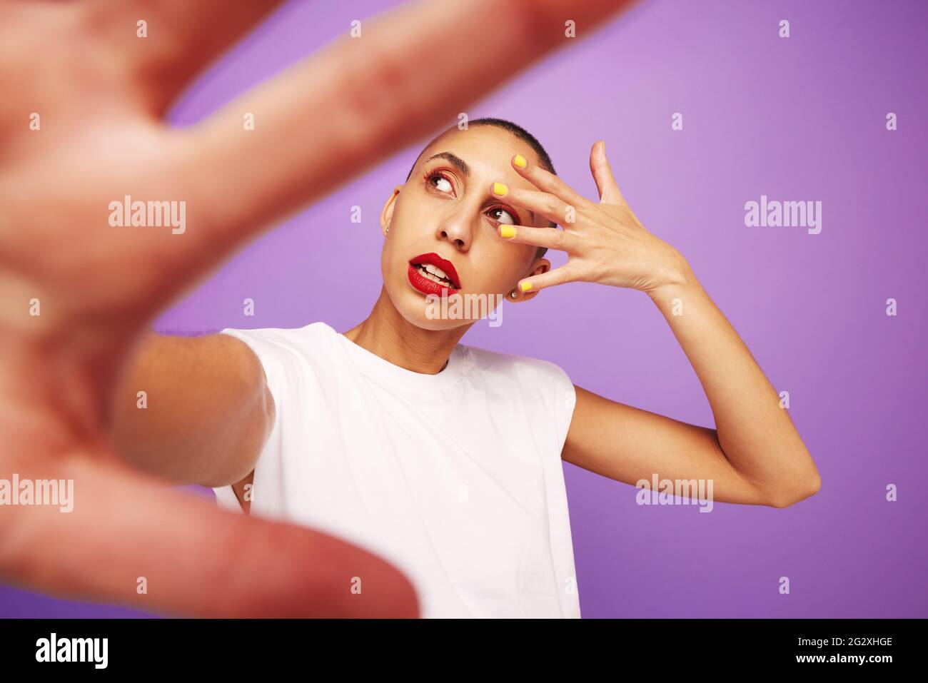 Femme mettant sa main devant l'appareil photo et l'autre devant son visage. Modèle féminin avec maquillage sur fond violet. Banque D'Images