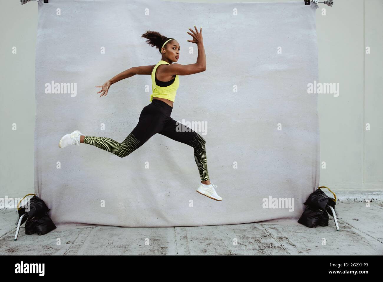 Jeune femme athlete en vetements de sport avec la coupe du corps saut en plein air. African sportswoman faire de la course a pied et de la fente exercice mi air pleine longueur