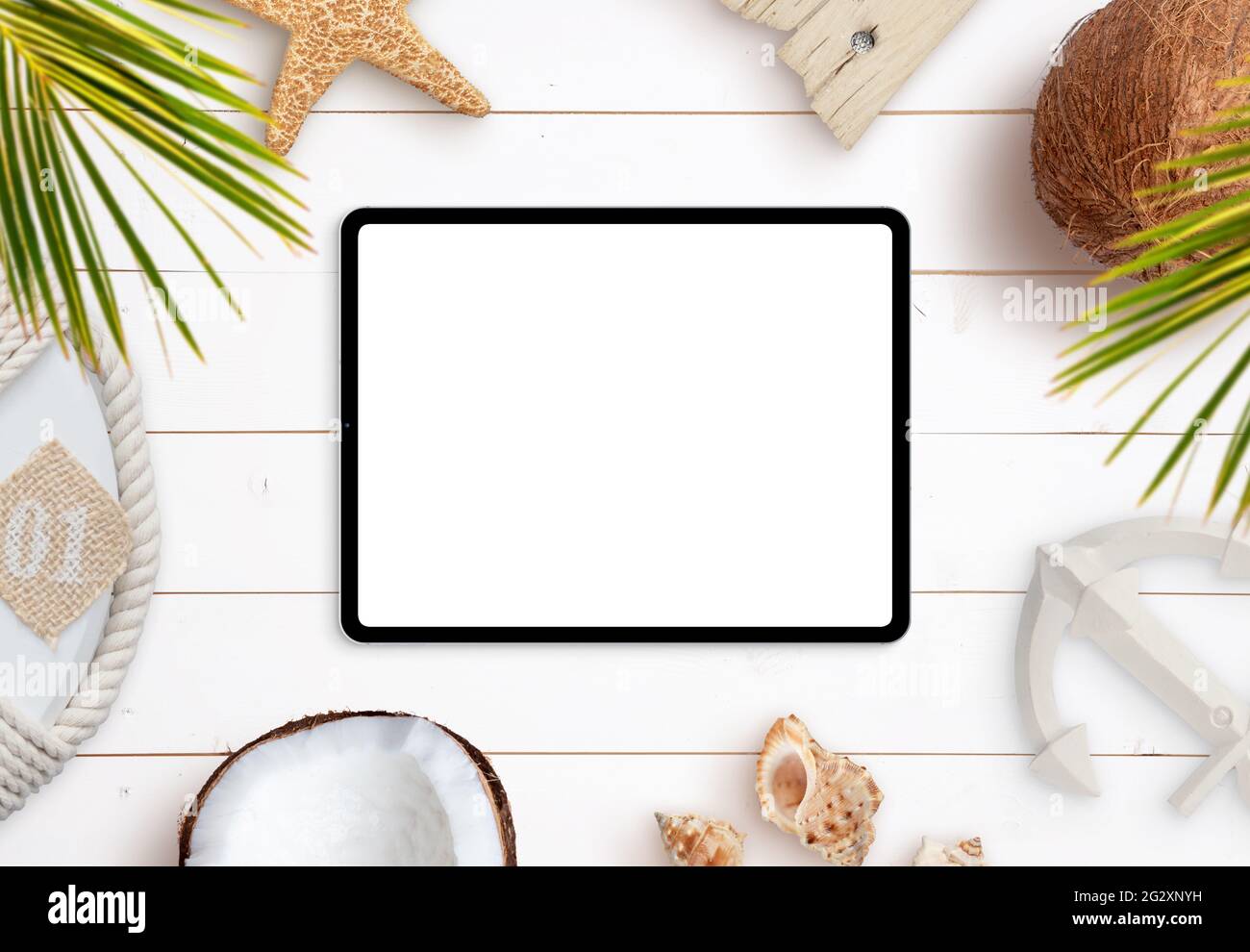 Maquette de tablette sur un bureau en bois blanc entouré de feuilles de palmier, d'étoiles de mer, de coquillages, de noix de coco, de ceintures de sauvetage et d'ancre. Été, voyage, vue de dessus, plat être Banque D'Images