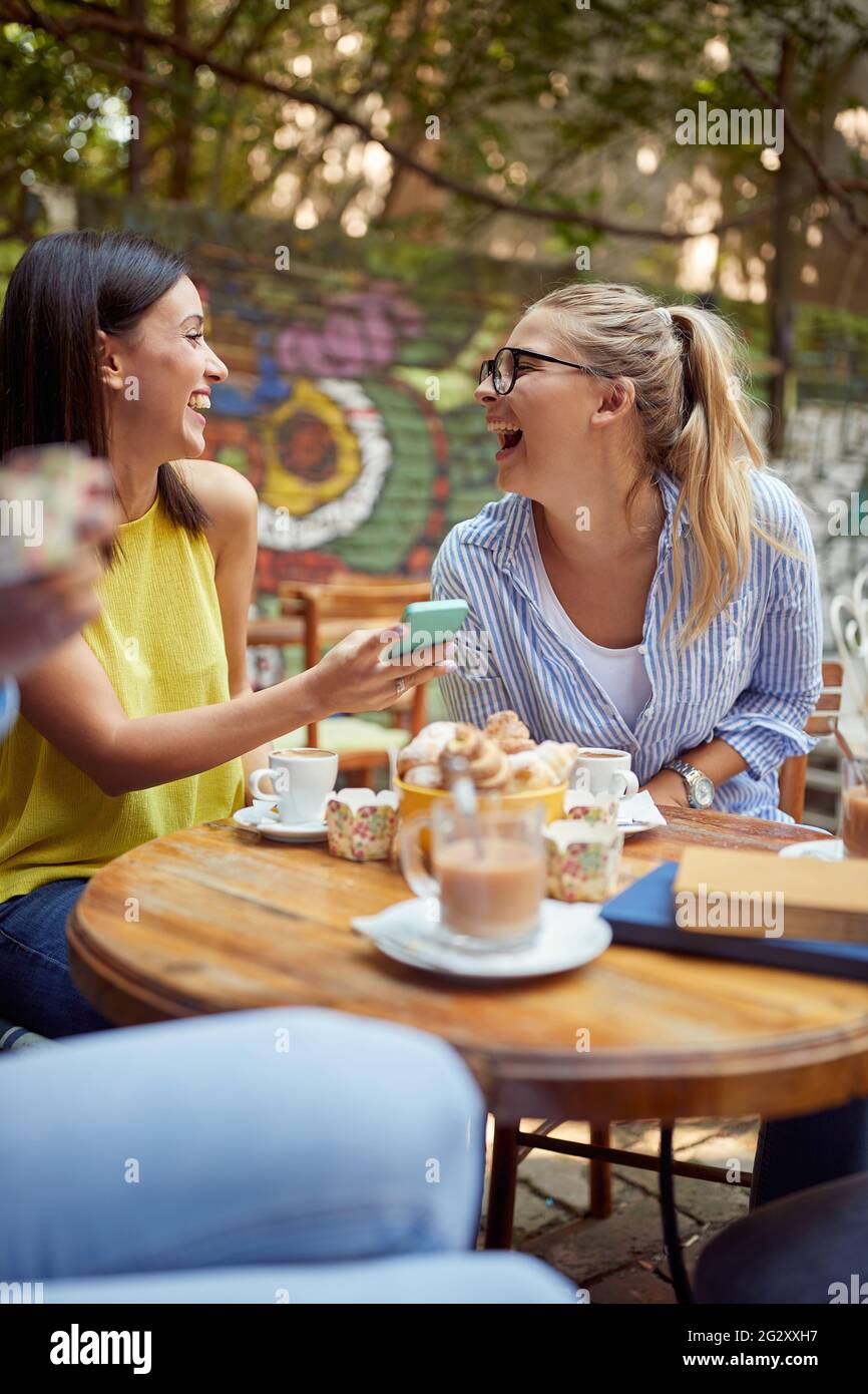 jeune femme de race blanche montrant du contenu sur son téléphone cellulaire à son amie, riant Banque D'Images