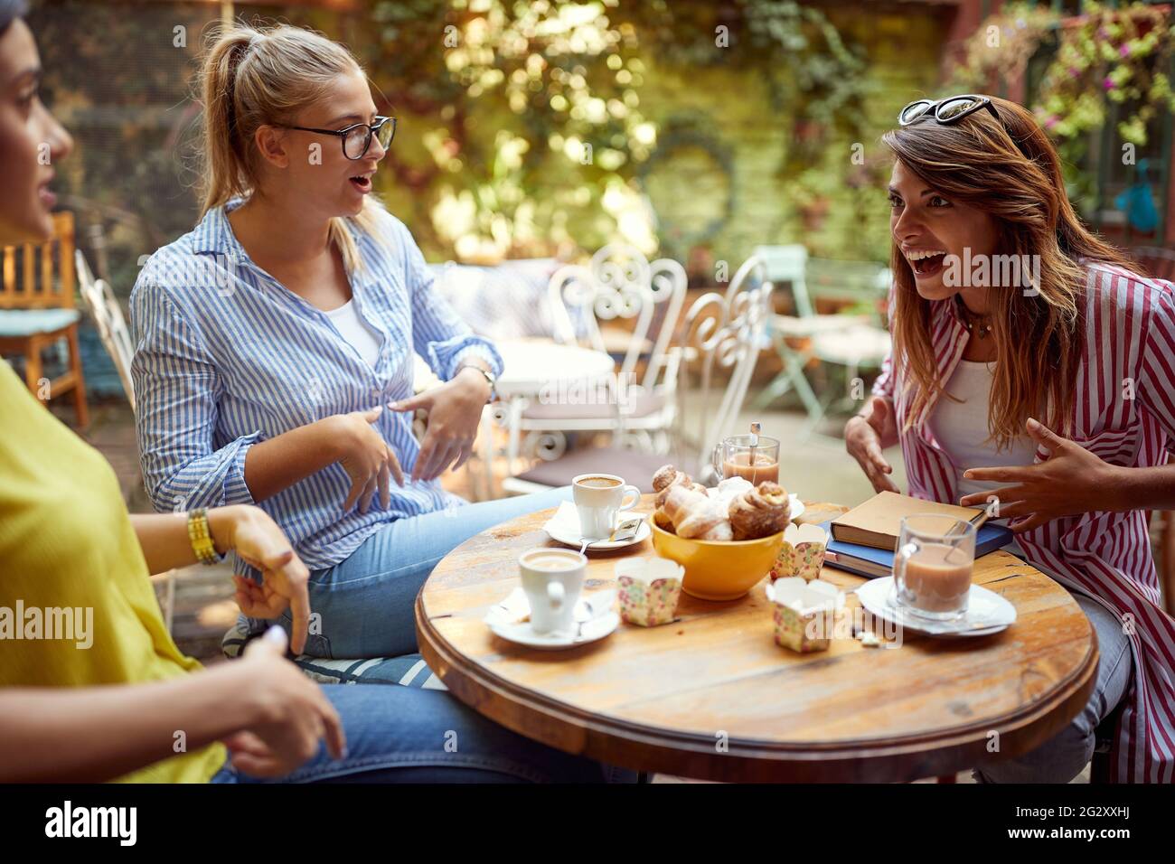 groupe d'amis caucasiens parlant dans un café en plein air, montrant sur leur ventre, riant. Banque D'Images