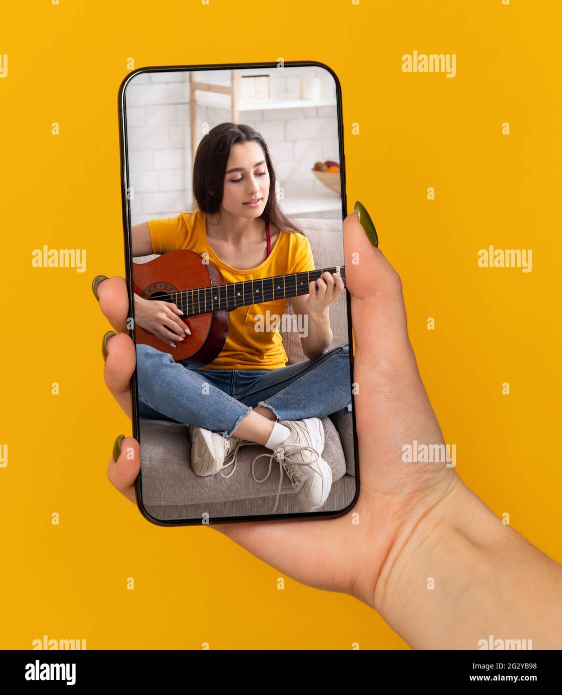Femme tenant un téléphone portable avec une leçon de musique en ligne à  l'écran, apprenant à jouer de la guitare sur le web, fond orange Photo  Stock - Alamy
