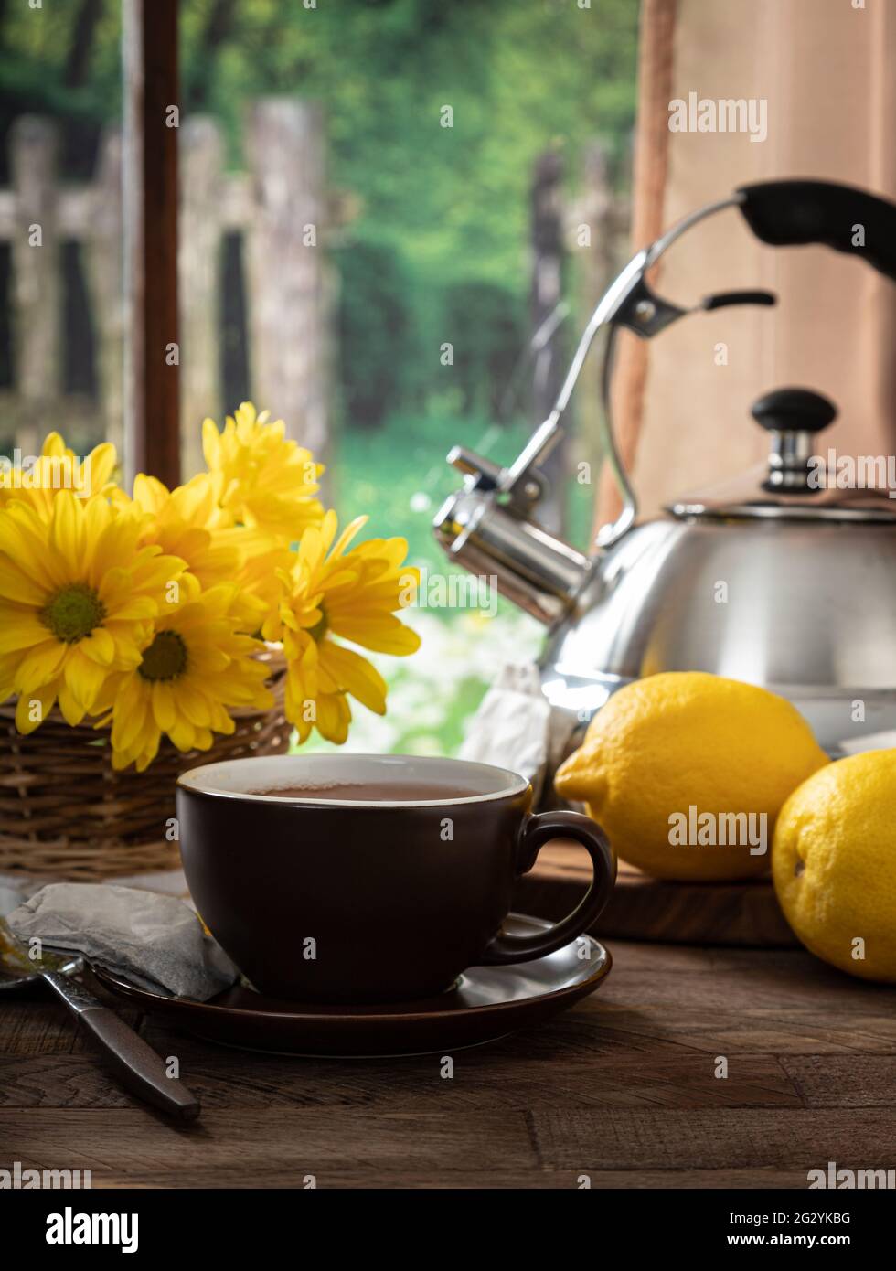 Tasse de thé avec citrons et fleurs sur une table en bois par une fenêtre à fond rural Banque D'Images