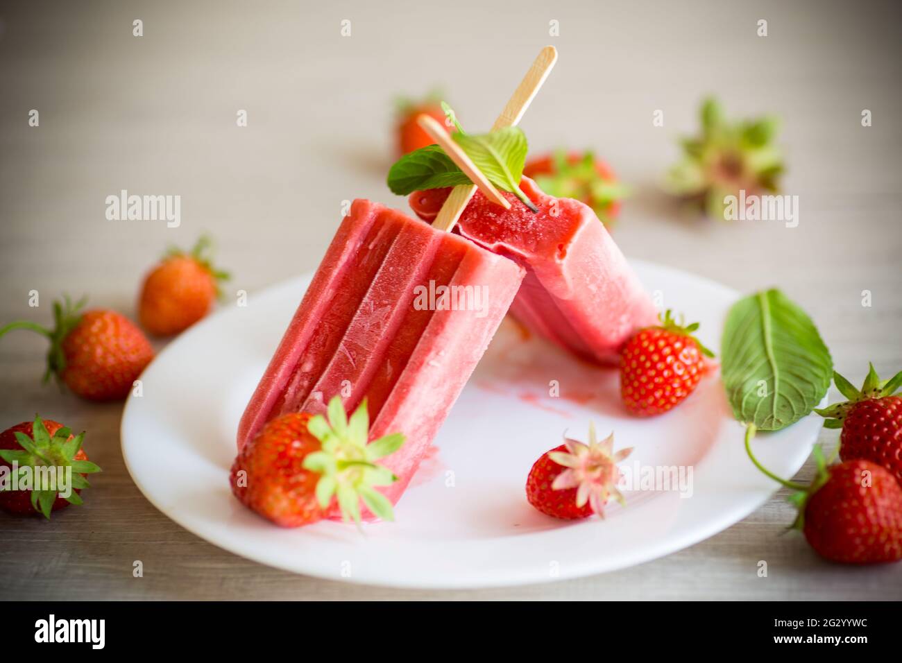 glace à la fraise maison sur un bâton fait à partir de fraises fraîches dans une assiette sur une table en bois Banque D'Images