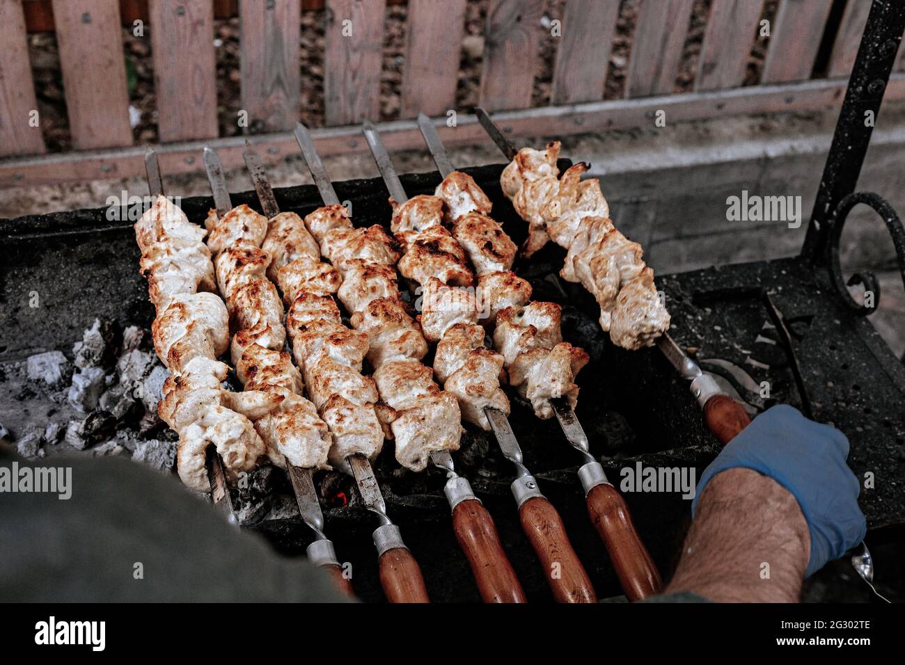 Le chef prépare le kebab au poulet. Cuisine de la rue turque. Viande cuite sur un feu, partie barbecue dans l'arrière-cour. Les mains mâles en gants tiennent une brochette en acier Banque D'Images