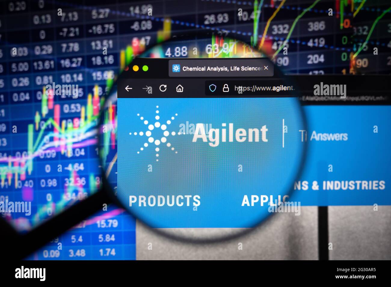 Le logo de la société Agilent sur un site web présentant des développements flous sur le marché boursier en arrière-plan, vu sur un écran d'ordinateur à travers une loupe Banque D'Images