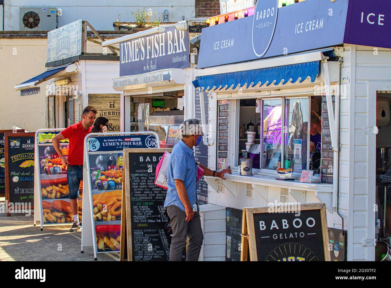 Les gens font la queue, socialement distancé, pour la glace et les Fish & chips, aux stands à emporter sur la plage de Lyme Regis, Jurassic Coast, Dorset, Angleterre Banque D'Images