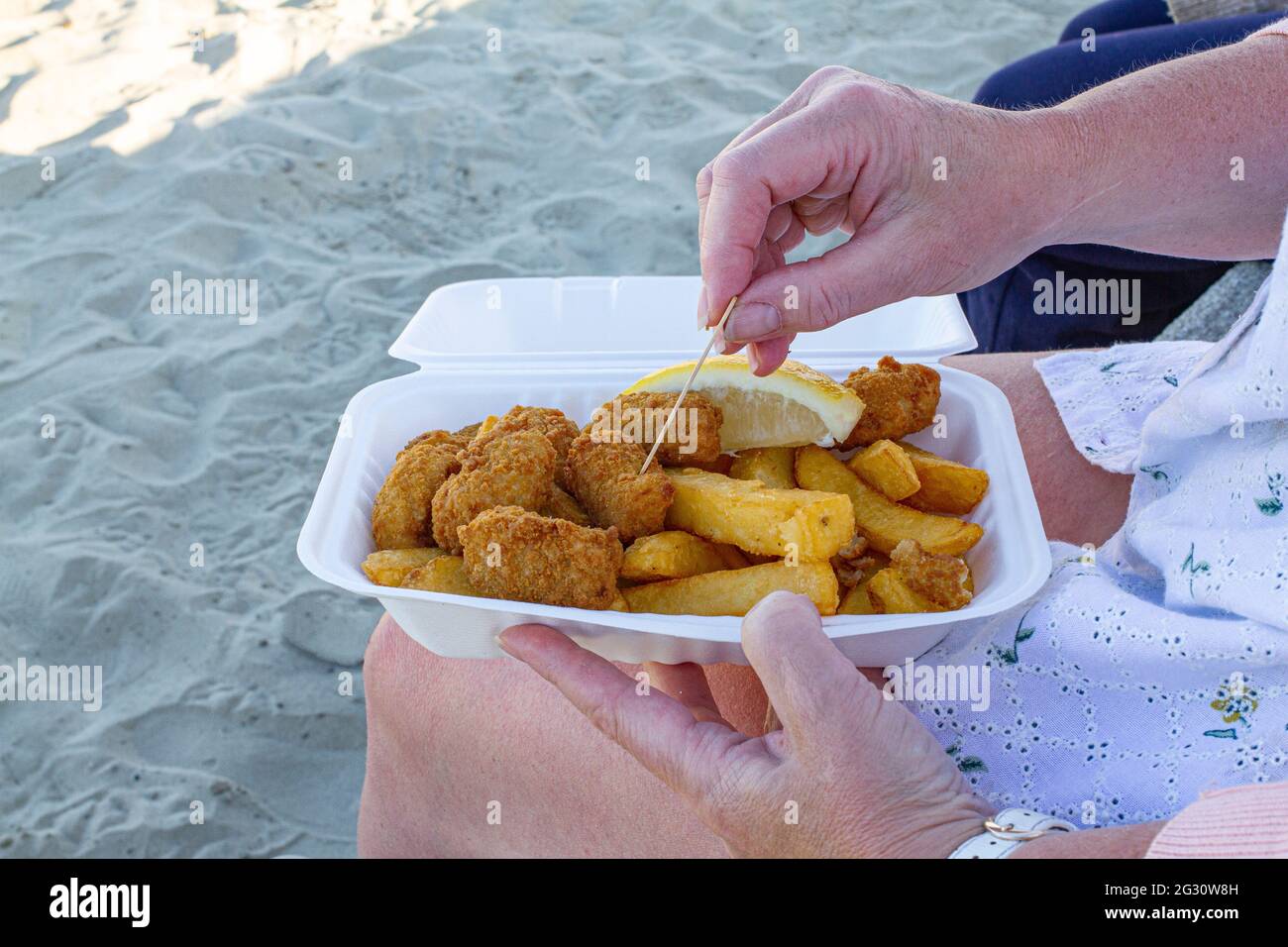 Gros plan d'une femme mangeant des scampi et des éclats d'un contenant en polystyrène, en utilisant une fourchette en bois, sur la plage à Lyme Regis, Dorset, Angleterre Banque D'Images