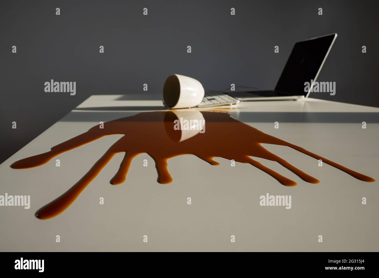 Une tasse de café noir a été renversé sur un ordinateur portable, sur un bureau blanc. Banque D'Images Une tasse de café noir a été renversé sur un ordinateur portable, sur un bureau blanc. Banque D'Images