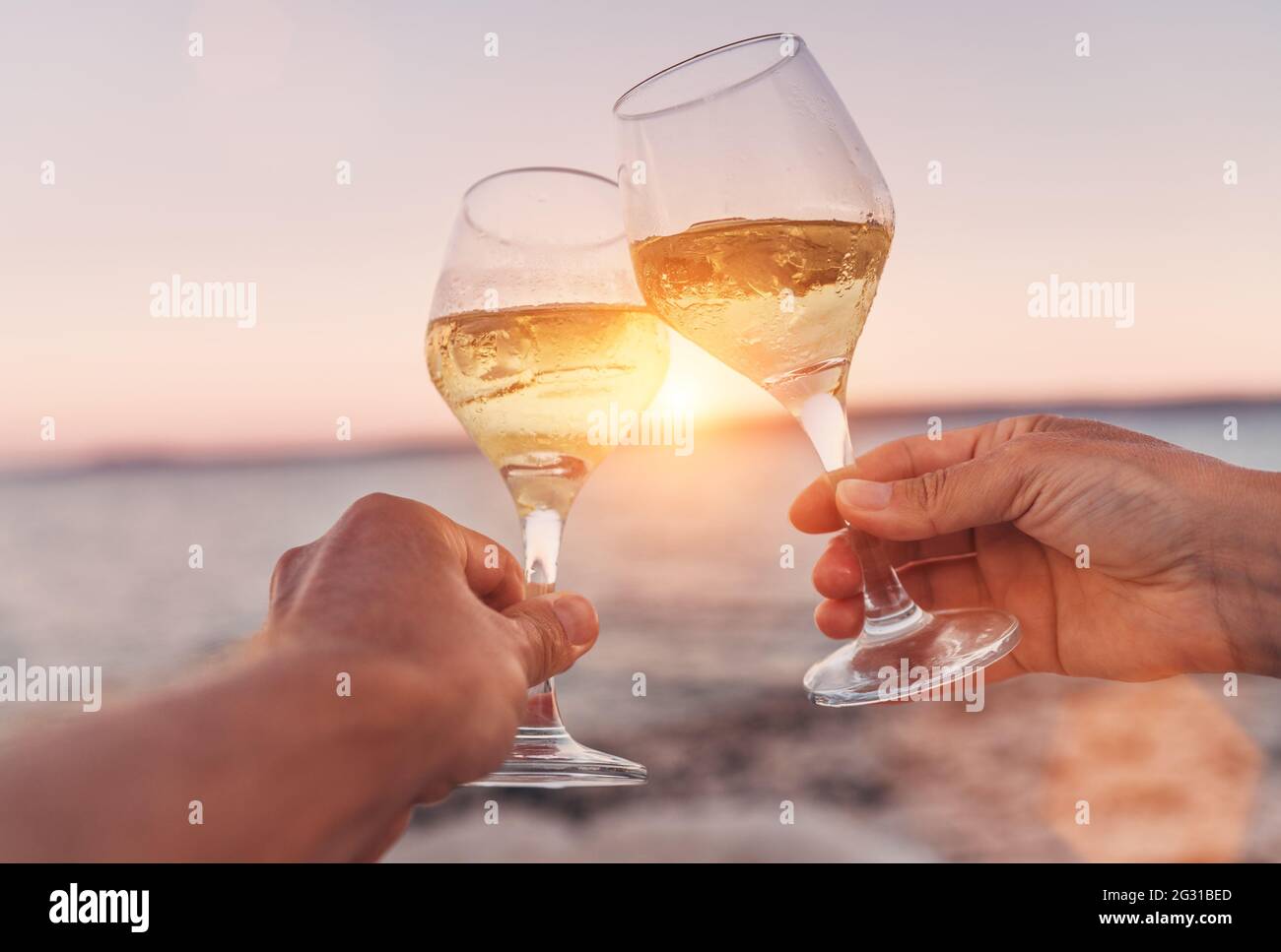 Couple amoureux se clinquant avec des verres à vin blanc pendant qu'ils  apprécient le beau coucher de soleil rose de bord de mer. Vacances  romantiques ou concept de datation en gros plan