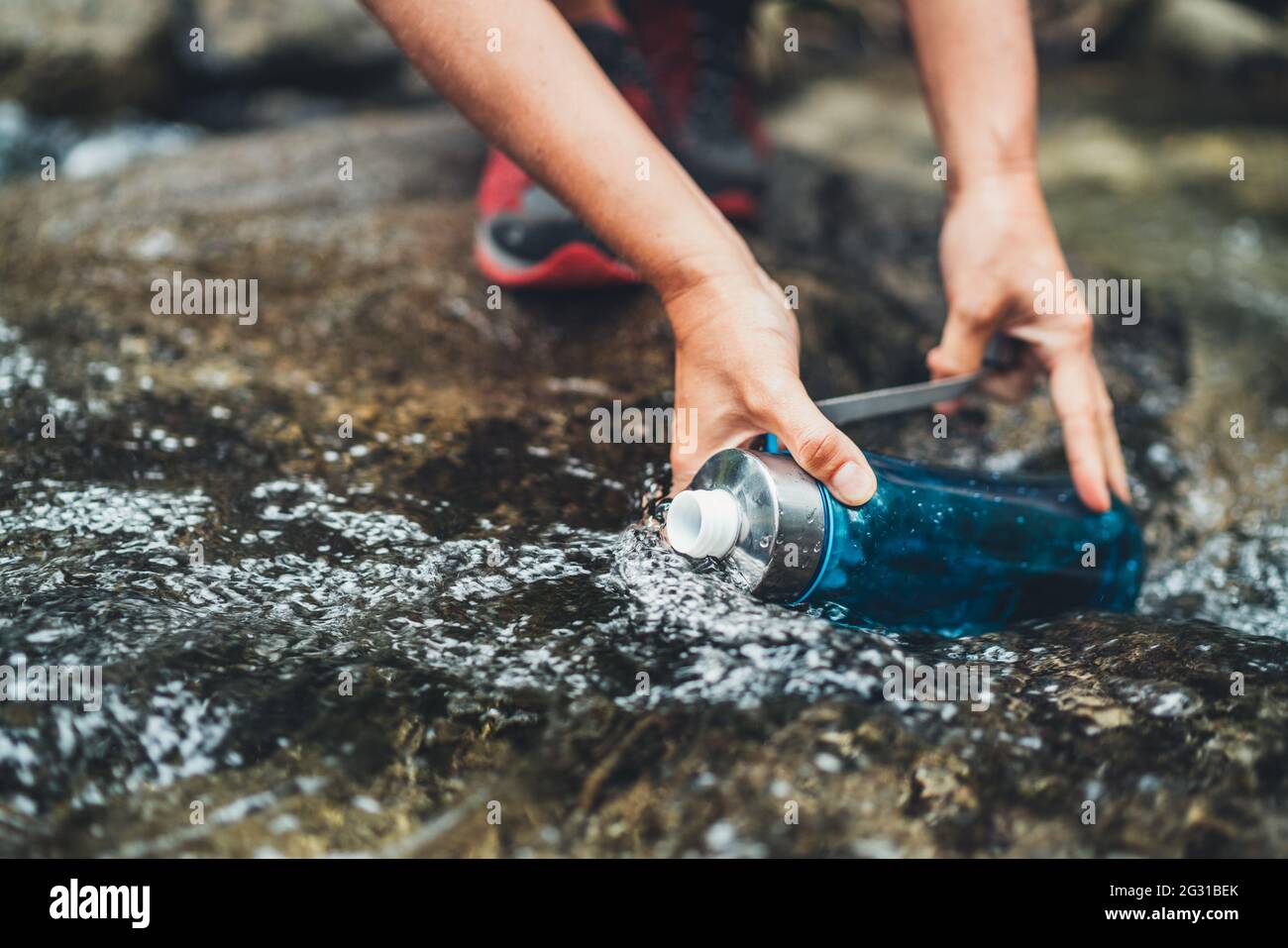 Photo en gros plan des mains de femmes remplissant un ruisseau de montagne frais dans la bouteille touristique en plastique pendant que l'eau se brise sur la randonnée touristique Banque D'Images