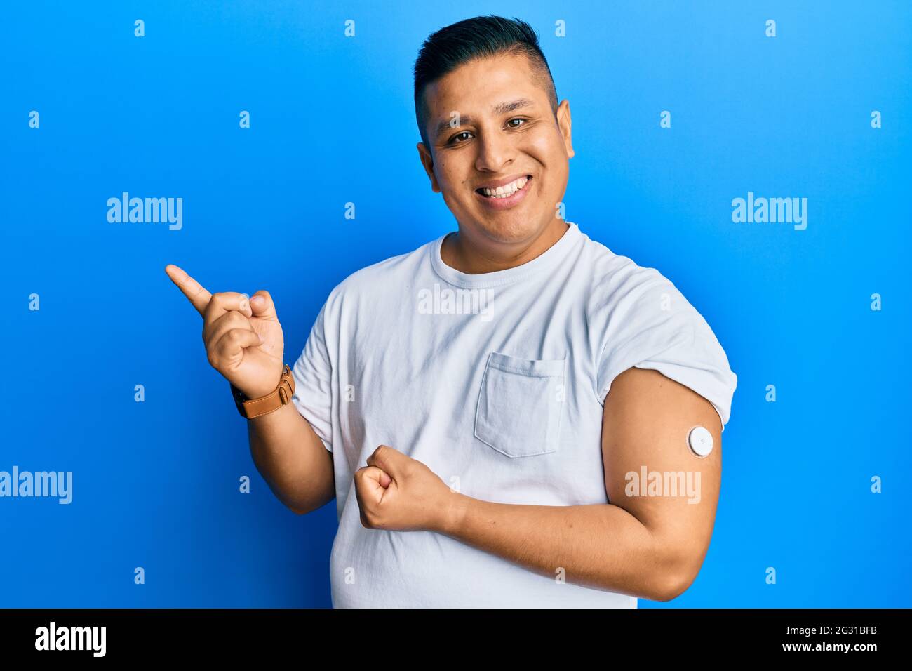 Jeune homme latin utilisant le bouton du glucomètre sourire heureux pointant avec la main et le doigt sur le côté Banque D'Images