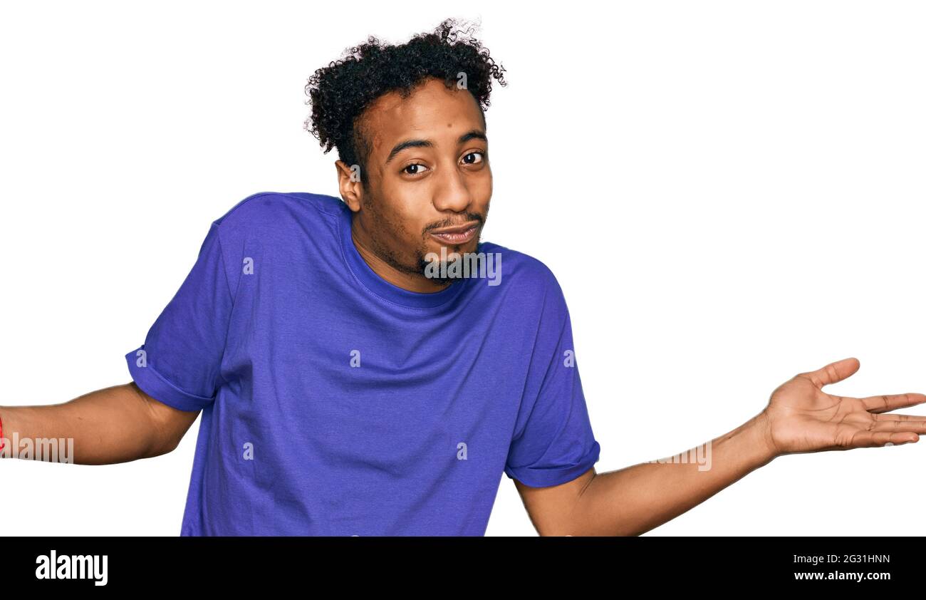 Jeune africain américain avec barbe portant un t-shirt violet décontracté expression sans indice et confuse avec les bras et les mains soulevées. Doute concept. Banque D'Images