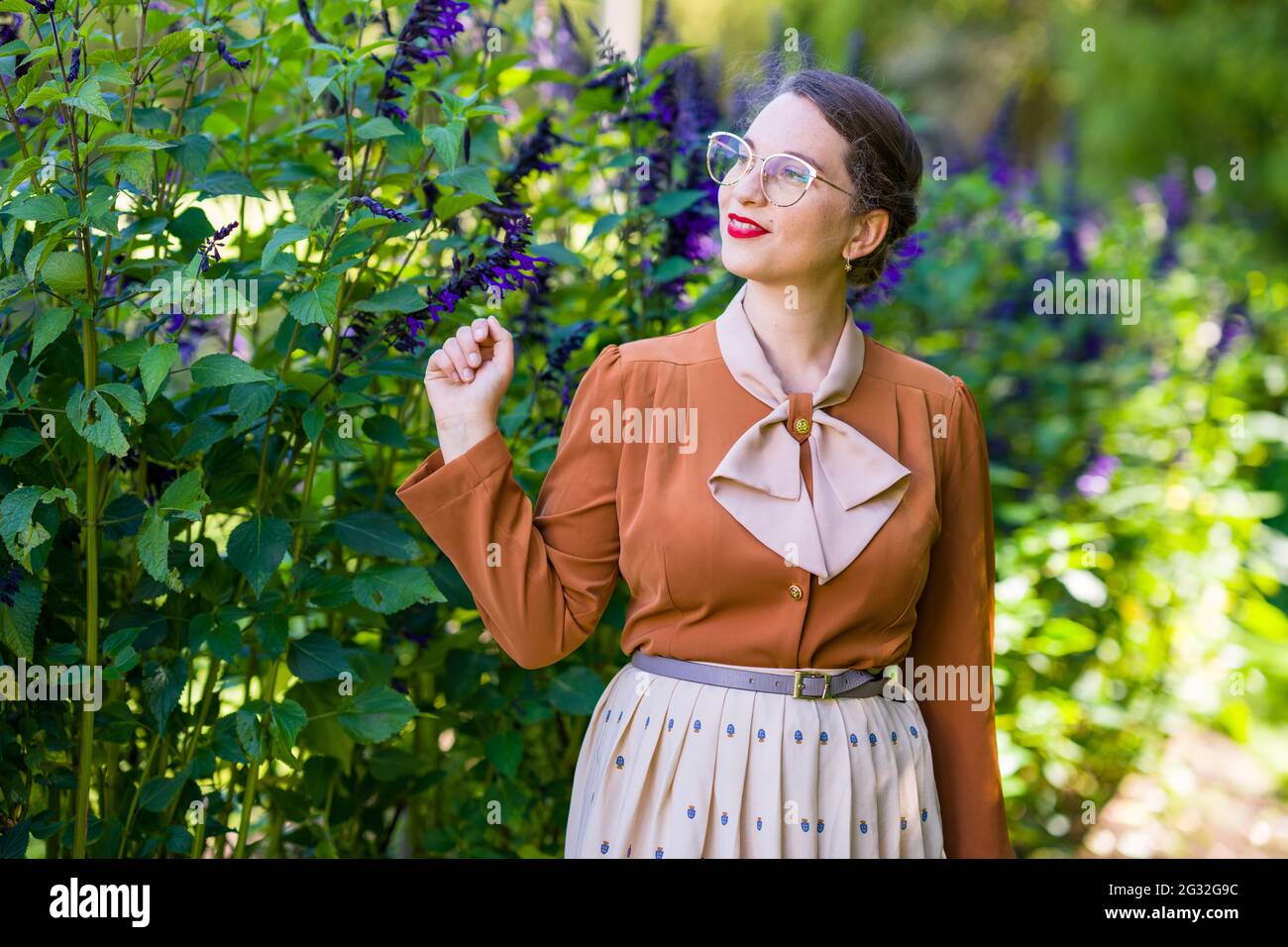 Jeune femme intellectuelle vêtue de vêtements des années 1940 dans un jardin Banque D'Images