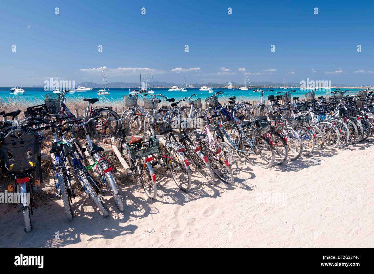 Vélos garés sur une plage sur l'île méditerranéenne de Formentera. En arrière-plan, le ciel bleu et les voiliers amarrés Banque D'Images