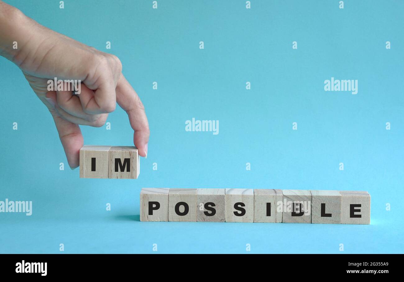 Retirez à la main le cube en bois avec le mot impossible à possible. Sur fond bleu. Banque D'Images