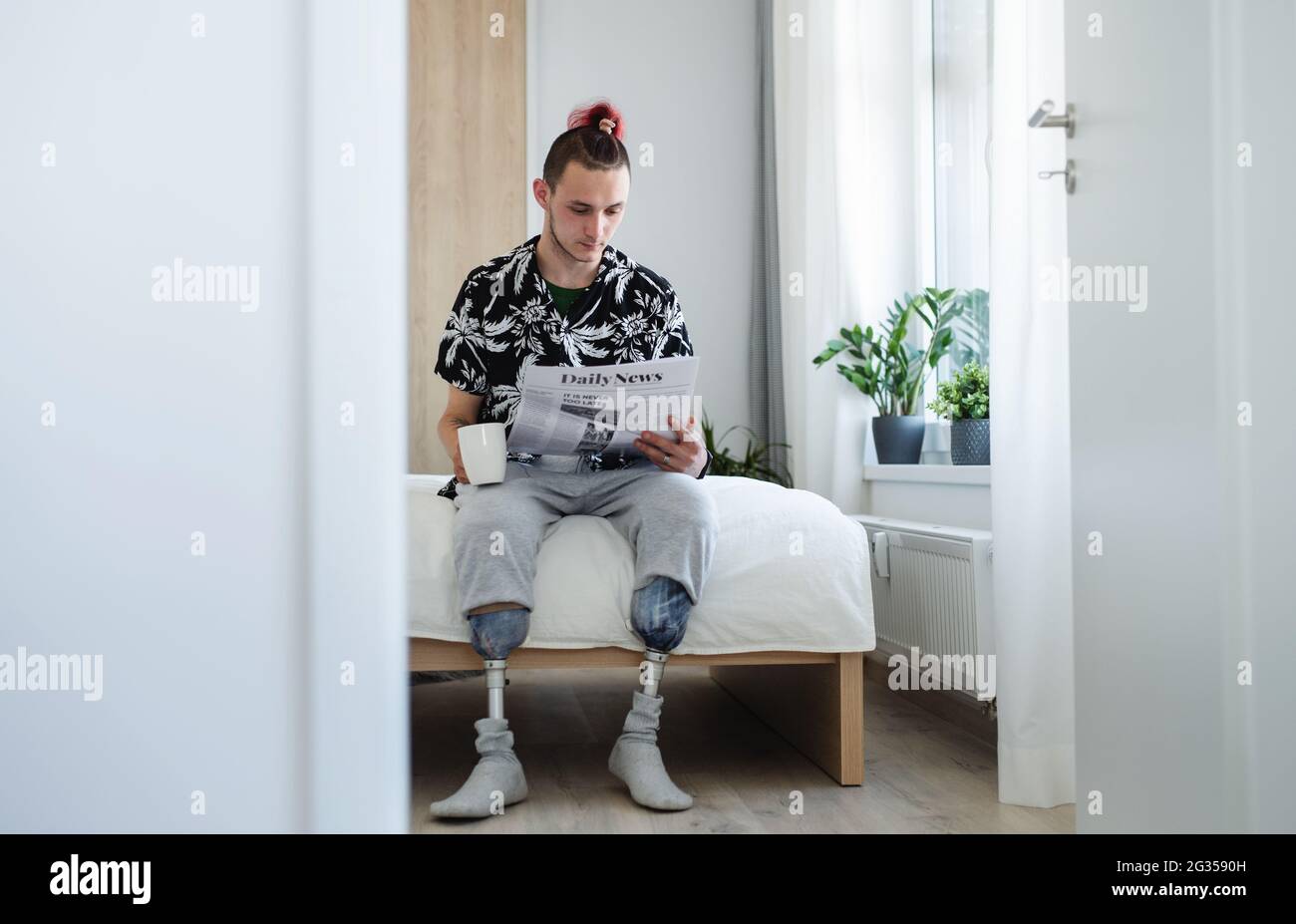 Portrait d'un jeune homme handicapé lisant des journaux au lit à l'intérieur à la maison, concept prothétique de jambe. Banque D'Images