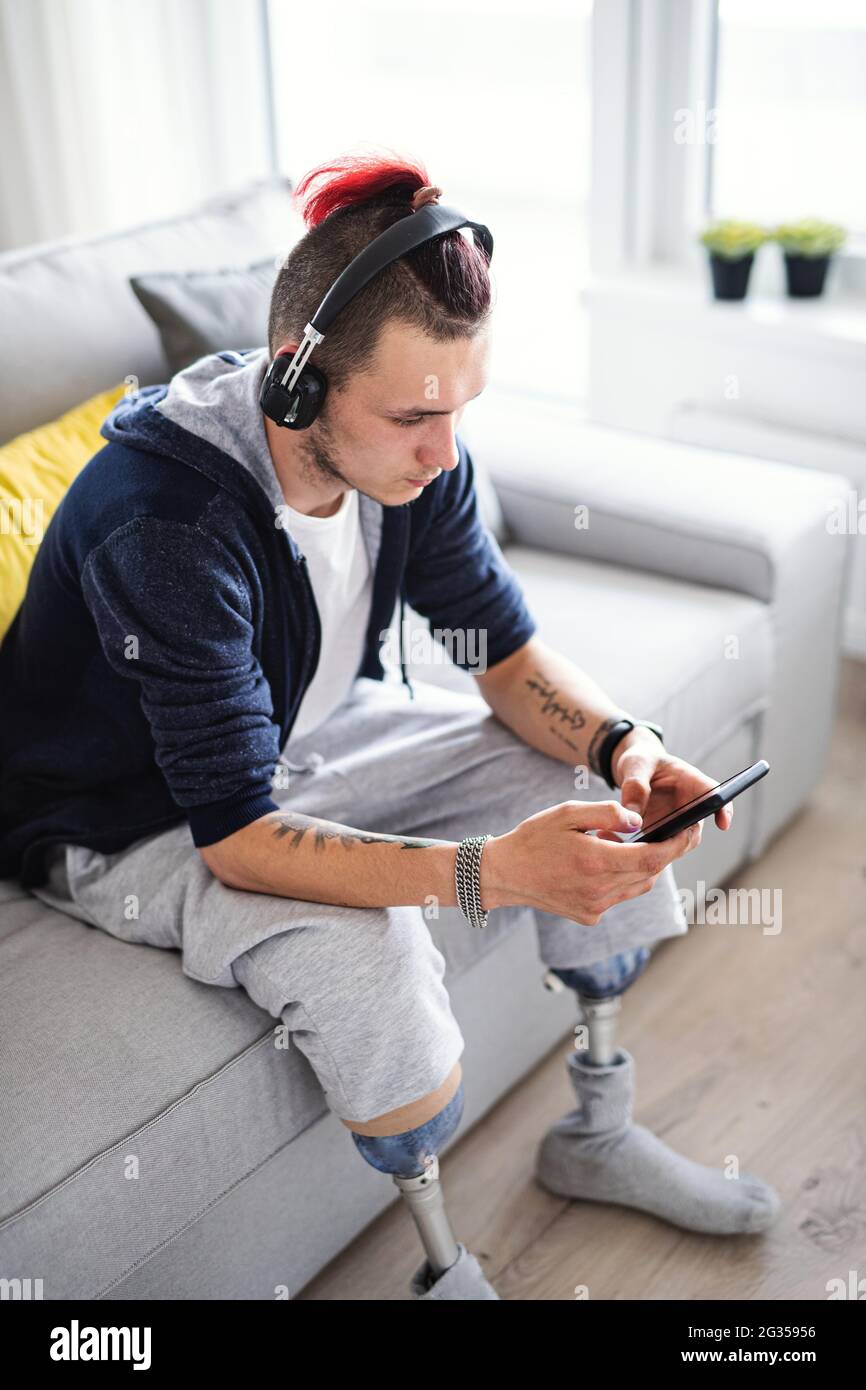 Portrait d'un jeune homme handicapé utilisant un smartphone à l'intérieur à la maison, concept de prothèse de jambe. Banque D'Images