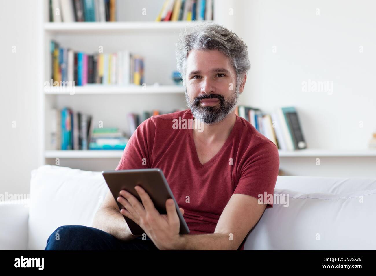 Homme adulte allemand mature lisant des nouvelles et des livres électroniques sur un ordinateur tablette à l'intérieur à la maison Banque D'Images