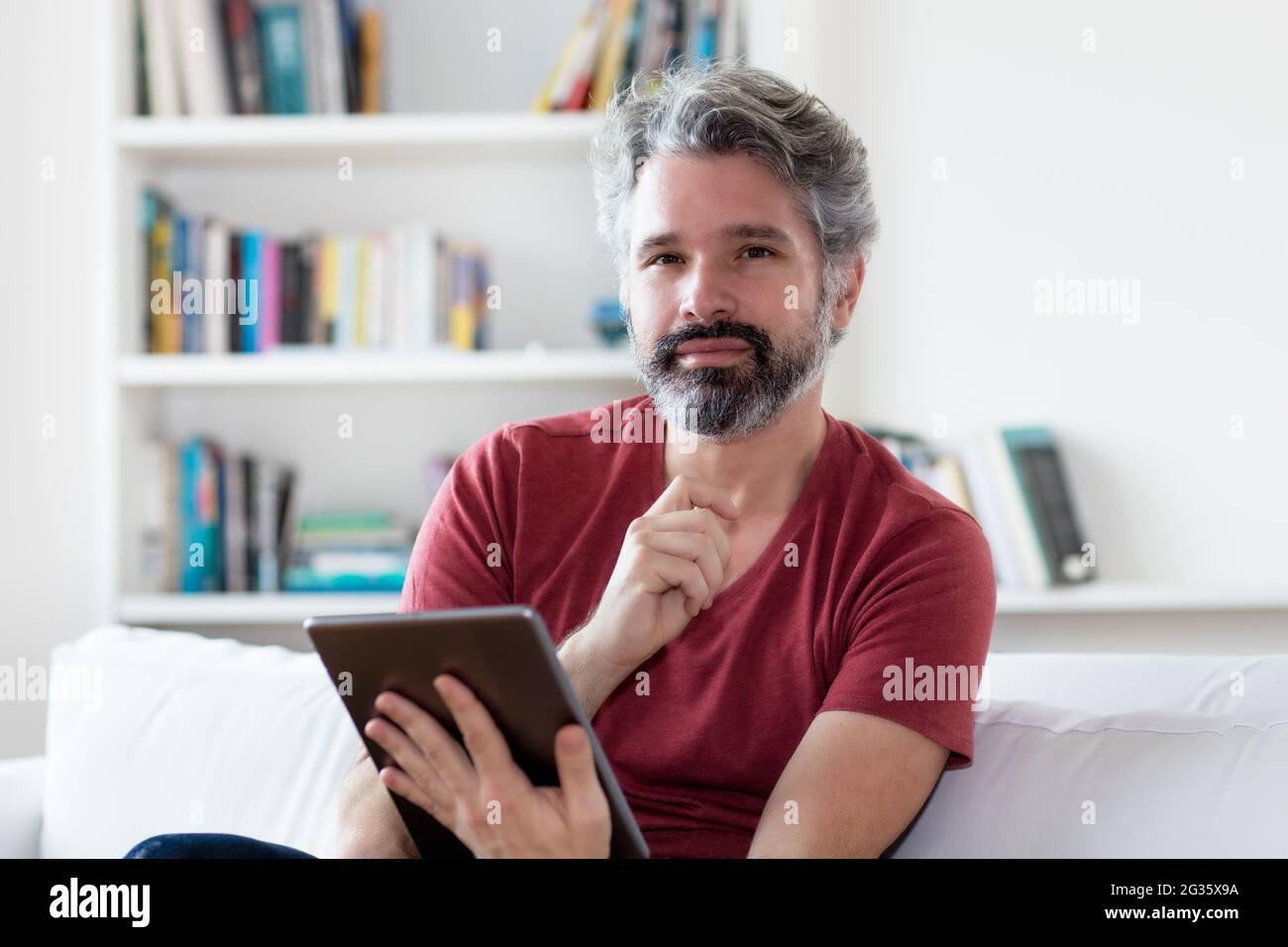 Beau homme adulte allemand mature lisant des nouvelles et des livres électroniques sur un ordinateur tablette à l'intérieur à la maison Banque D'Images