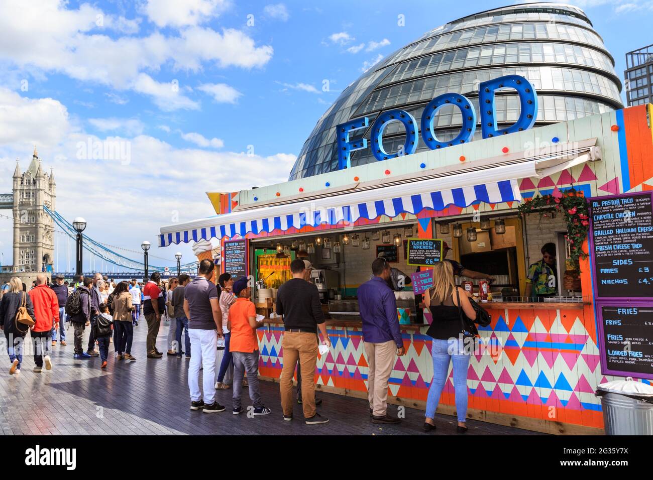 Les gens achètent de la nourriture dans des stands extérieurs pop up à plus de Londres sous le soleil d'été avec Tower Bridge et City Hall en arrière-plan, Londres, Angleterre Banque D'Images