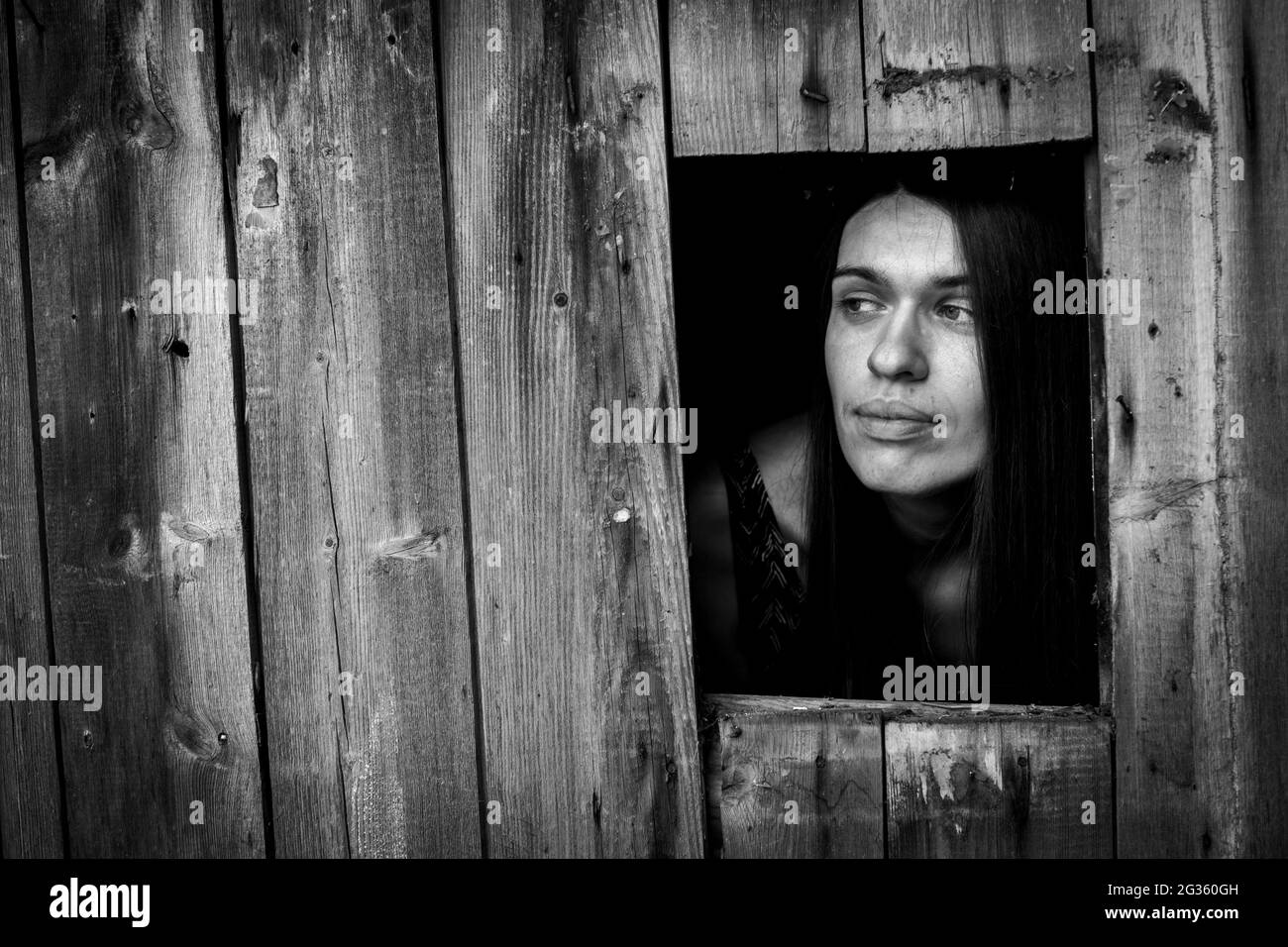 Une jeune femme dans un bâtiment en bois ща fenêtre. Photo en noir et blanc. Banque D'Images