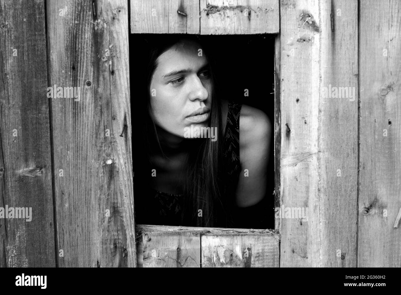 Une jeune femme dans une petite fenêtre. Photo en noir et blanc. Banque D'Images